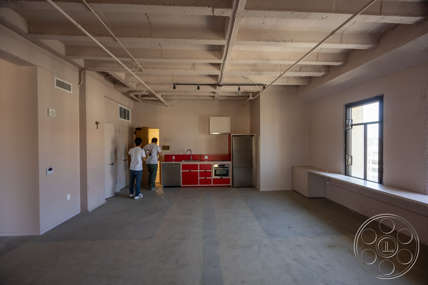 The Plaza - modern kitchen, large windows, minimalist design, open floor plan, concrete floor, industrial style, urban setting, floor-to-ceiling windows, neutral wall color, exposed concrete ceiling, stainless steel refrigerator, seamless cabinetry, integrated kitchen appliances, red kitchen cabinetry