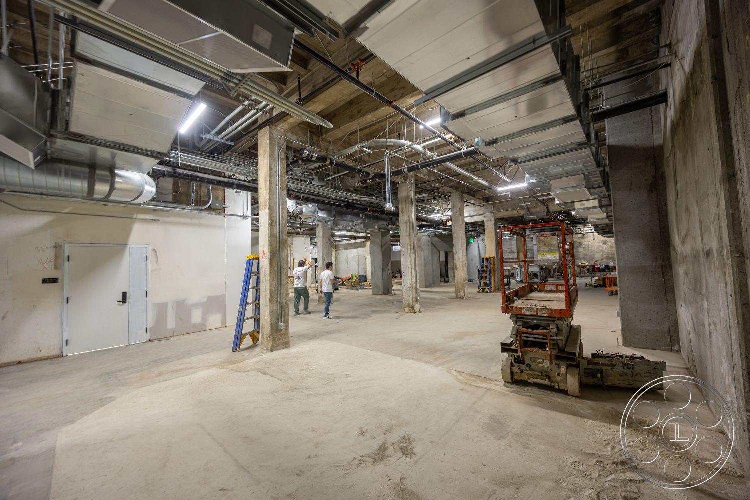 The Plaza - open floor plan, exposed concrete walls, industrial lighting fixtures, steel structural columns, metal ductwork ceiling, utility room, concrete support beams, mechanical room, unfinished concrete flooring, construction site interior