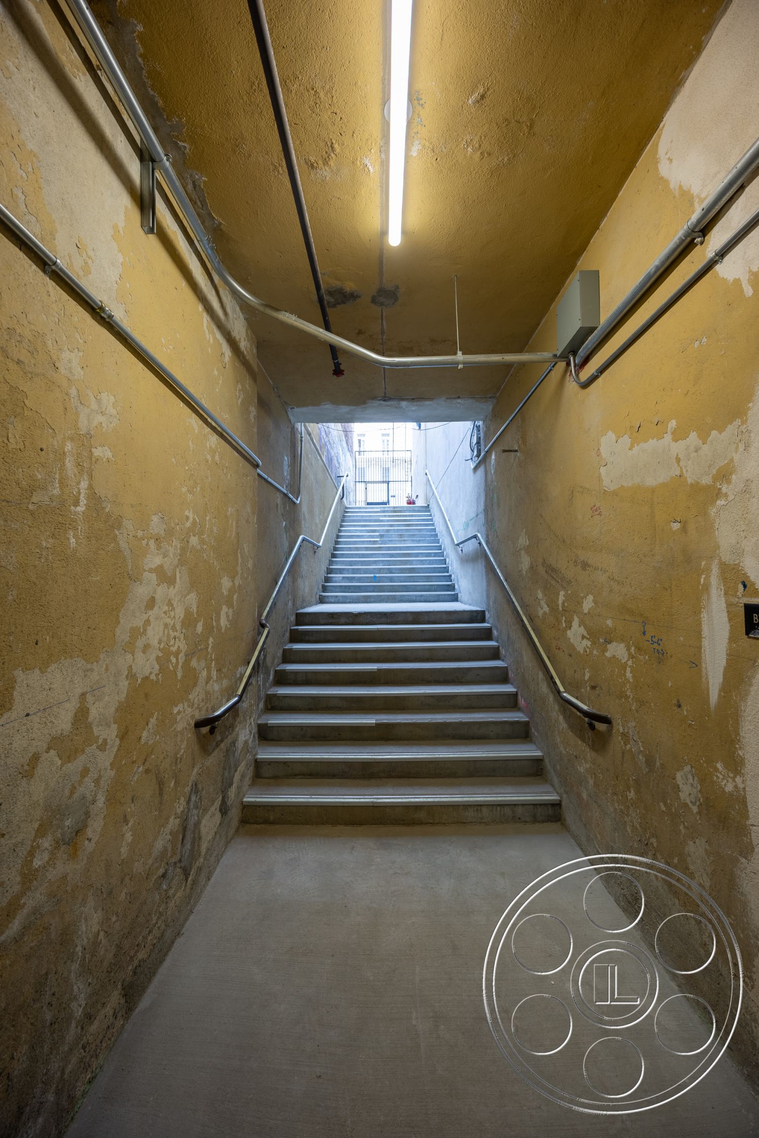 The Plaza - exterior, concrete floor, industrial lighting, textured plaster walls, metal handrail, exposed piping, yellow painted walls, concrete staircase, rectangular stairway