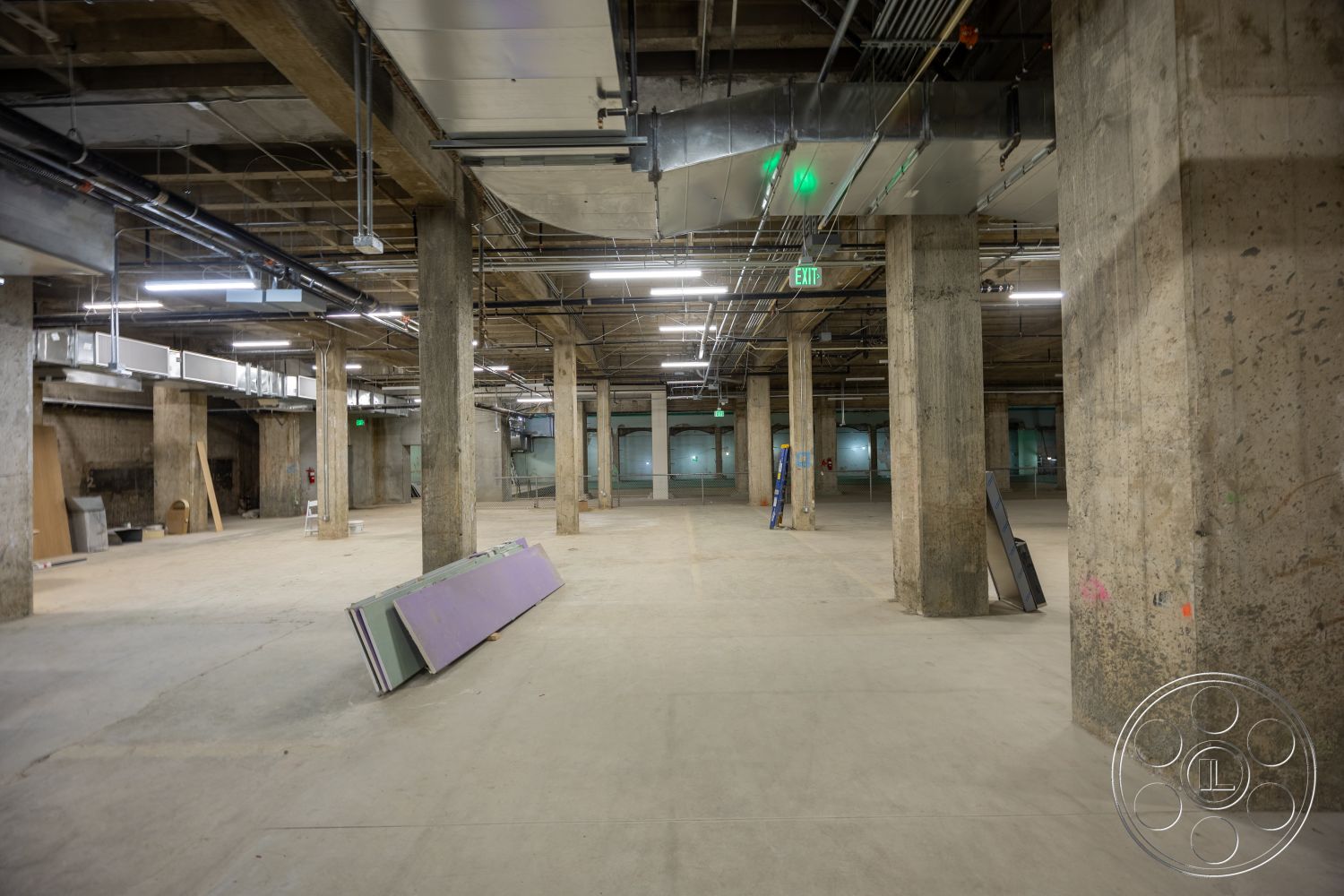 The Plaza - open floor plan, concrete floor, industrial lighting fixtures, metal ductwork, unfinished interior, exposed concrete columns, exit signage, ceiling beams, utility piping