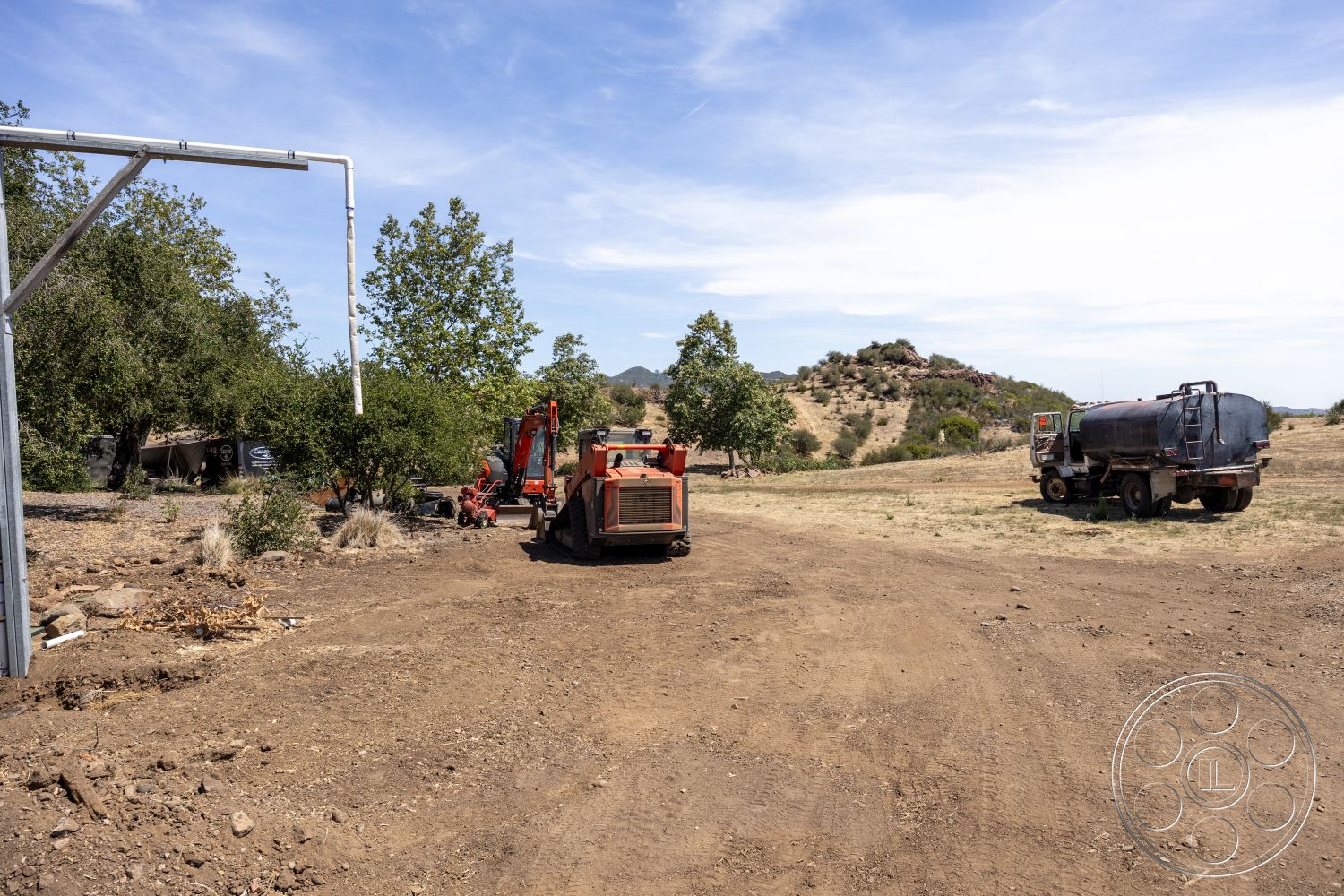 Eagle Feather - exterior, vegetation, metal framework, rural setting, mountainous backdrop, construction equipment, open field, dirt landscape, orange tractor, tree surroundings, industrial vehicle