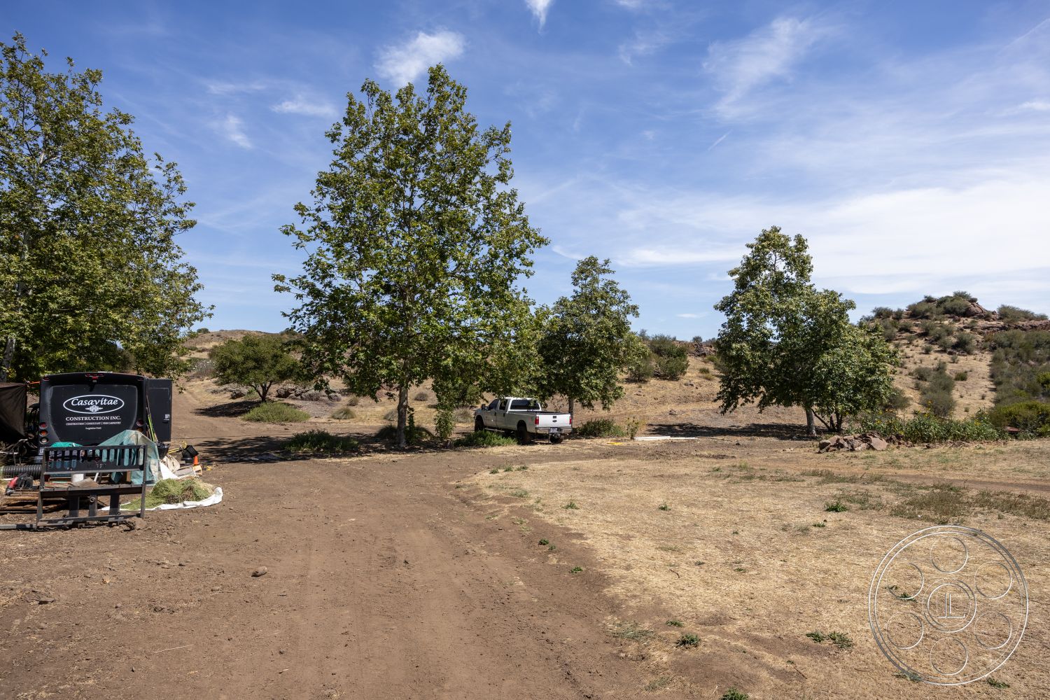 Eagle Feather - clear blue sky, deciduous trees, scattered shrubs, outdoor work area, pickup truck, dirt access road, dry landscape setting, construction trailer, natural hillside