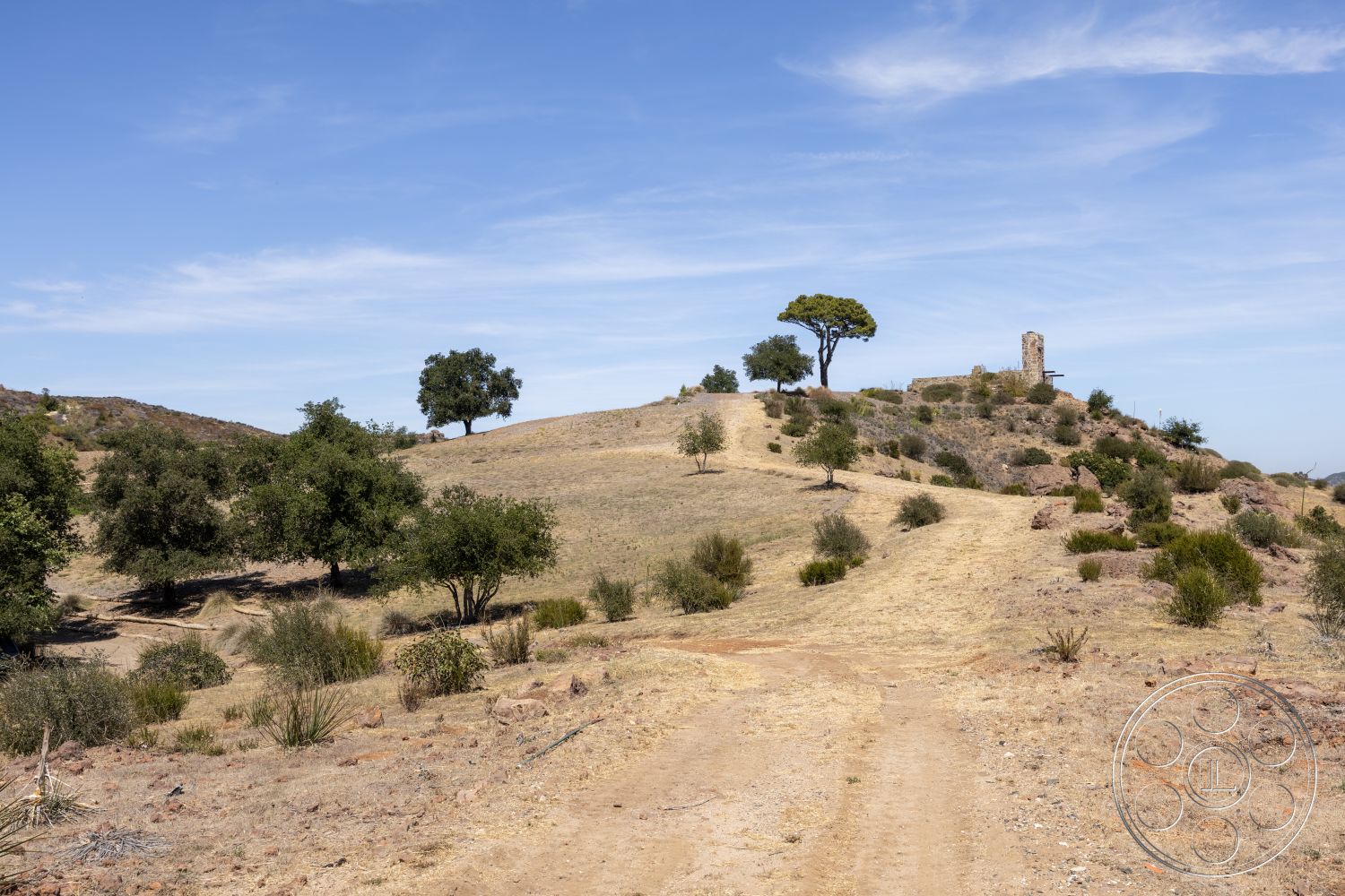 Eagle Feather - exterior, natural landscape, blue sky, distant hills, dirt pathway, undulating terrain, scattered trees, overgrown shrubs, rocky outcrop, historic tower structure, open grassland