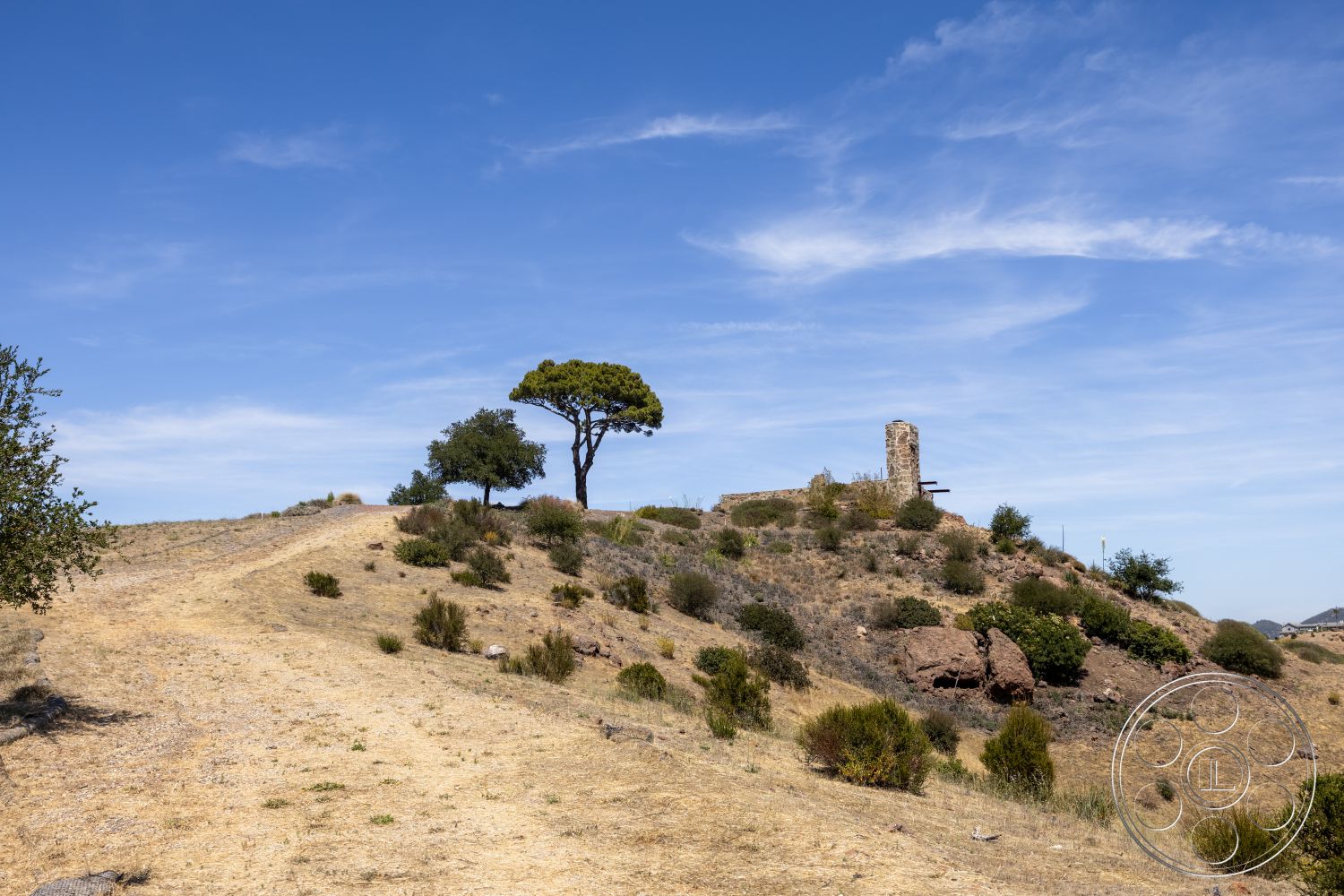Eagle Feather - exterior, desert landscape, rocky hillside, scattered shrubs, distant ruins, dry grasses, old stone structure, single pine tree, open blue sky