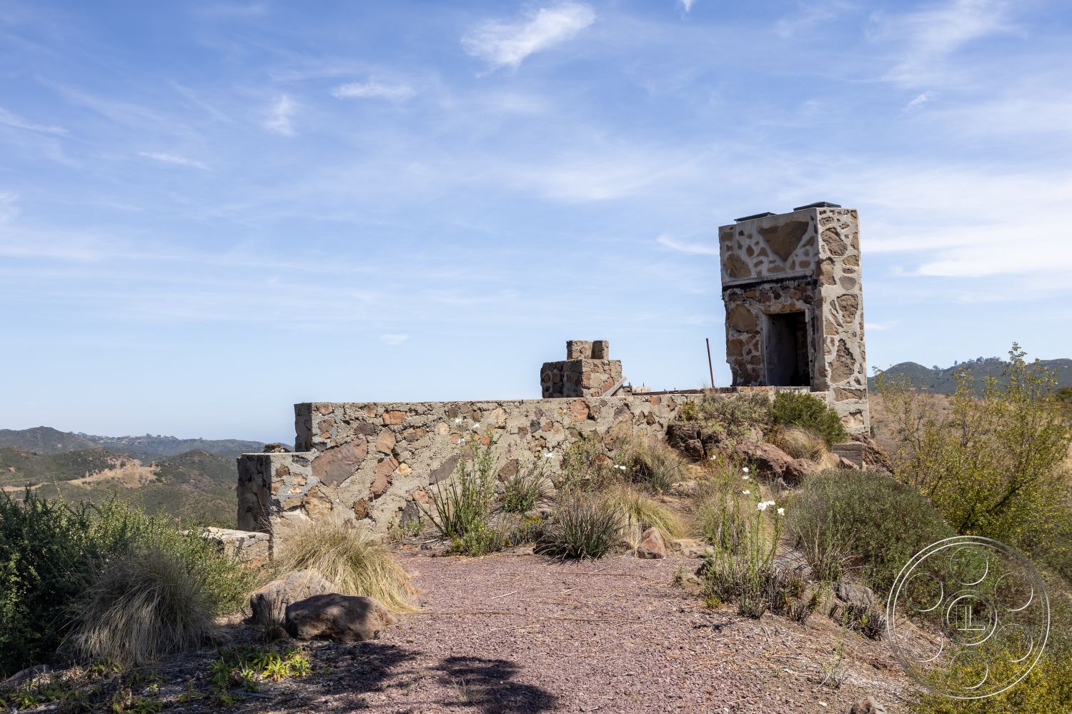 Eagle Feather - exterior, gravel pathway, desert landscape, surrounding mountains, natural hillside setting, stone wall construction, irregular shaped stone wall, stone chimney structure, partially ruined stone structure