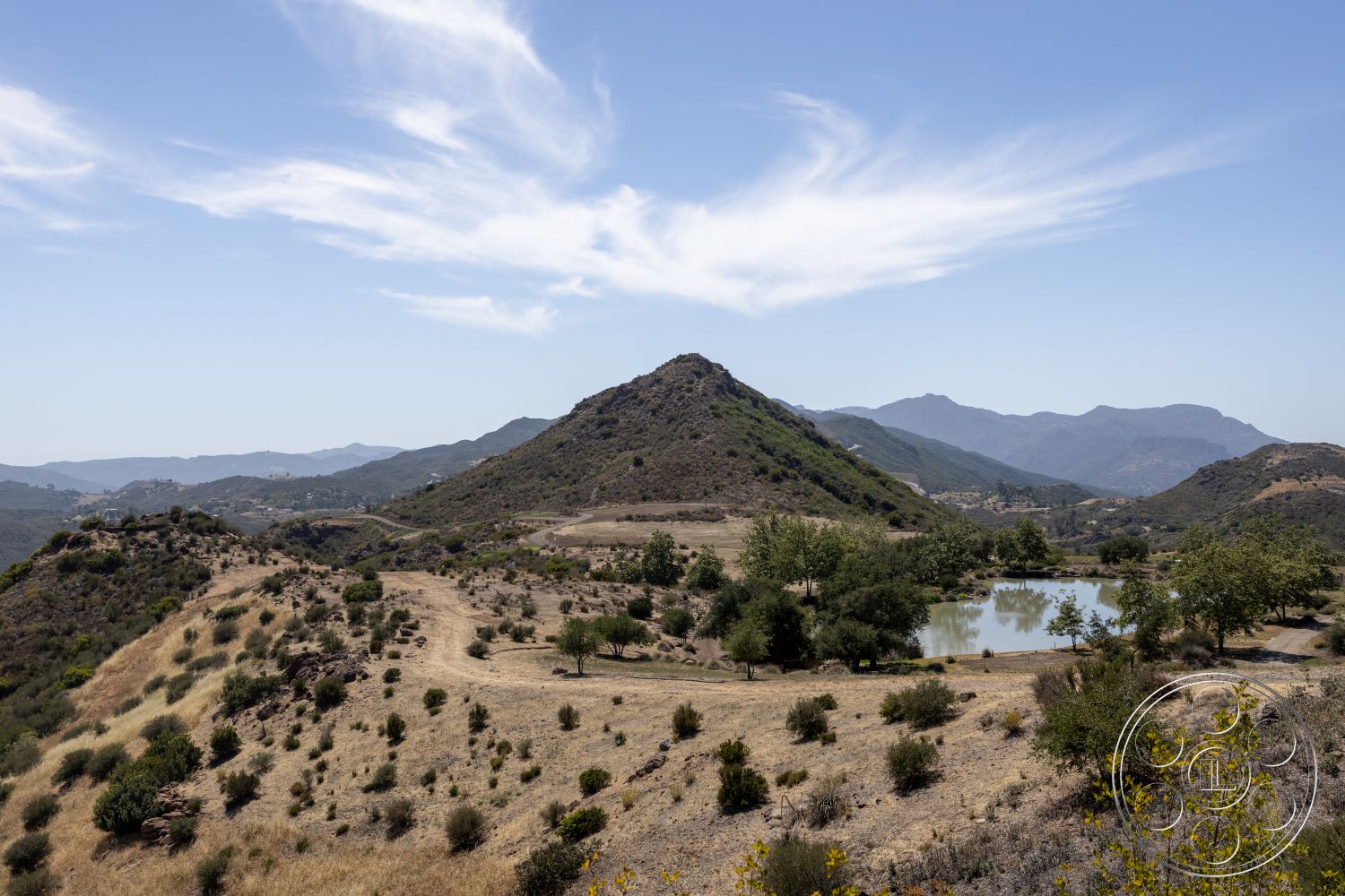 Eagle Feather - scenic view, natural landscape, clear blue sky, hillside location, scattered trees, dry grassland, pond, cloud formations, dense shrubs, mountain range