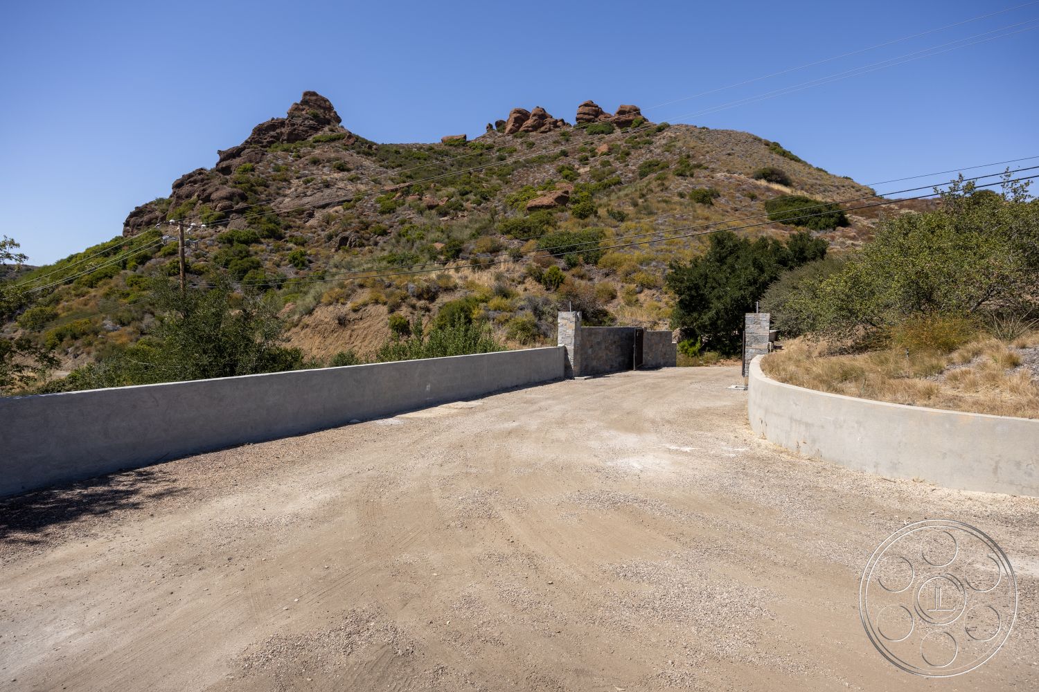 Eagle Feather - exterior, natural vegetation, surrounding trees, landscaped hillside, mountain backdrop, gate entrance, rocky terrain, dirt driveway, concrete boundary wall, gravel entrance