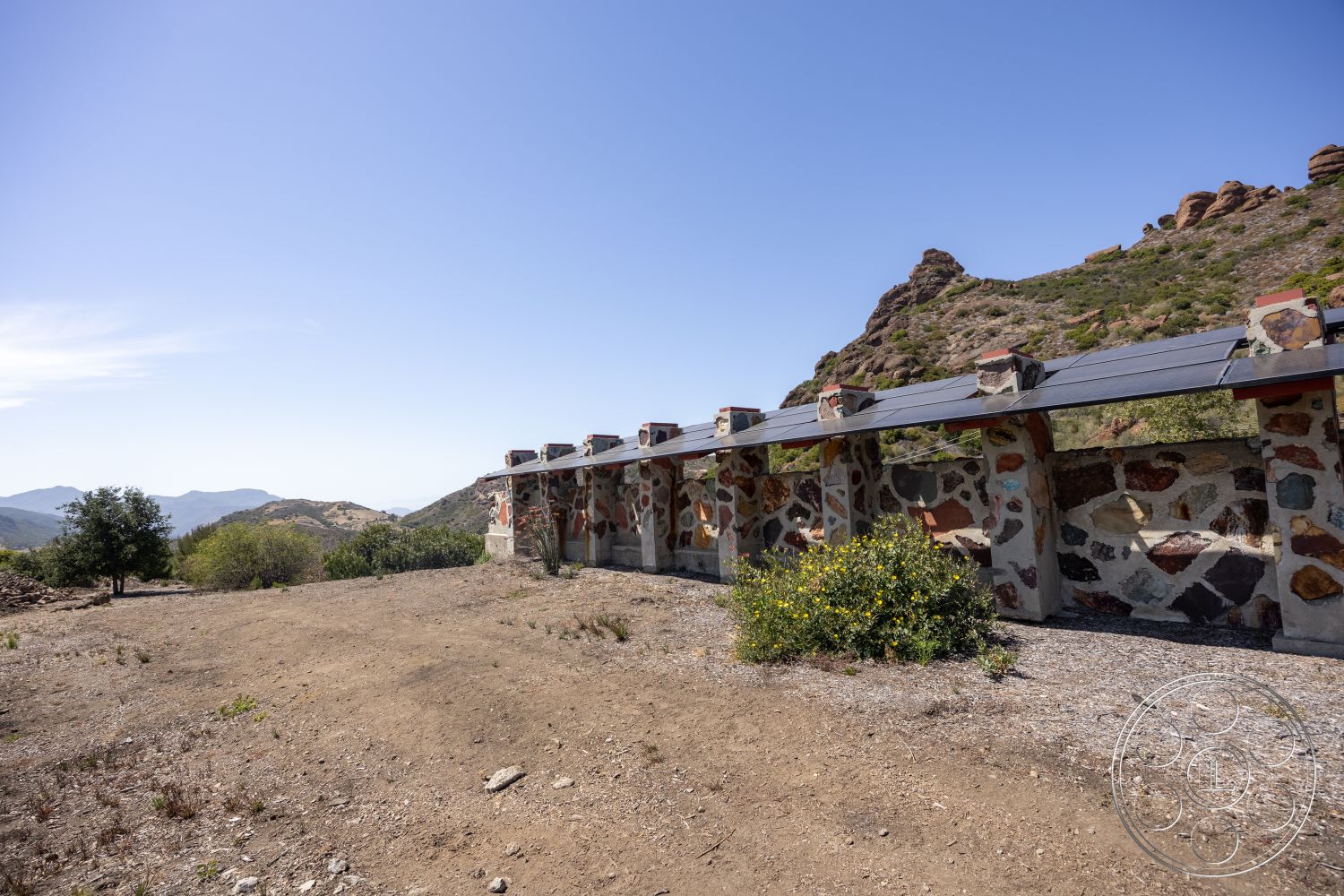 Eagle Feather - exterior, landscaped area, mountain view, gravel ground cover, open-air pavilion, solar panel roof, rustic architectural style, natural stone wall cladding, desert landscape setting, wooden beam roof structure, buildings with stone columns