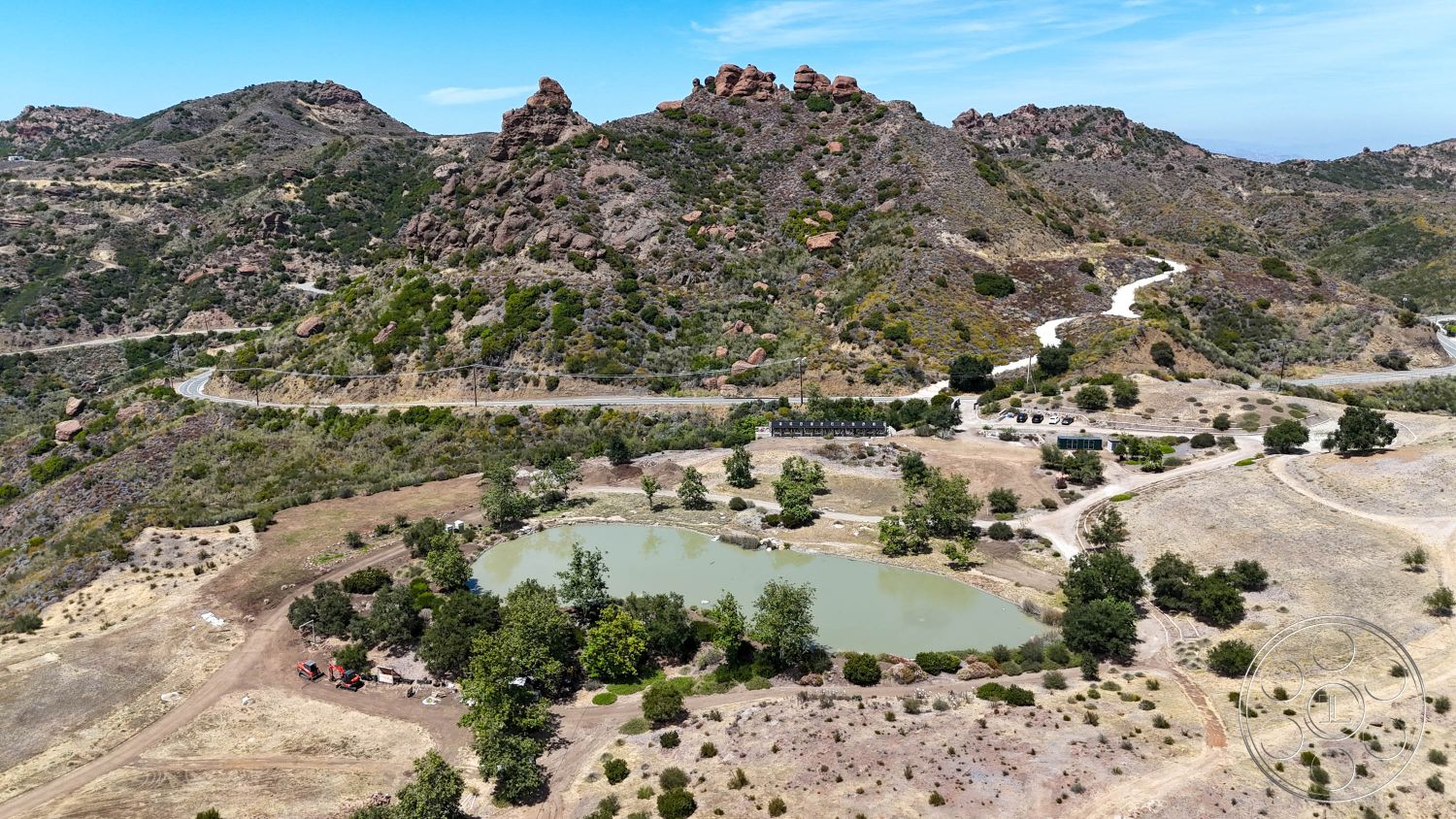 Eagle Feather - exterior, outdoor space, natural landscape, large trees, rural setting, undulating terrain, dirt pathways, scenic mountain backdrop, rocky hills, green wooded area, oval pond, arid grassland