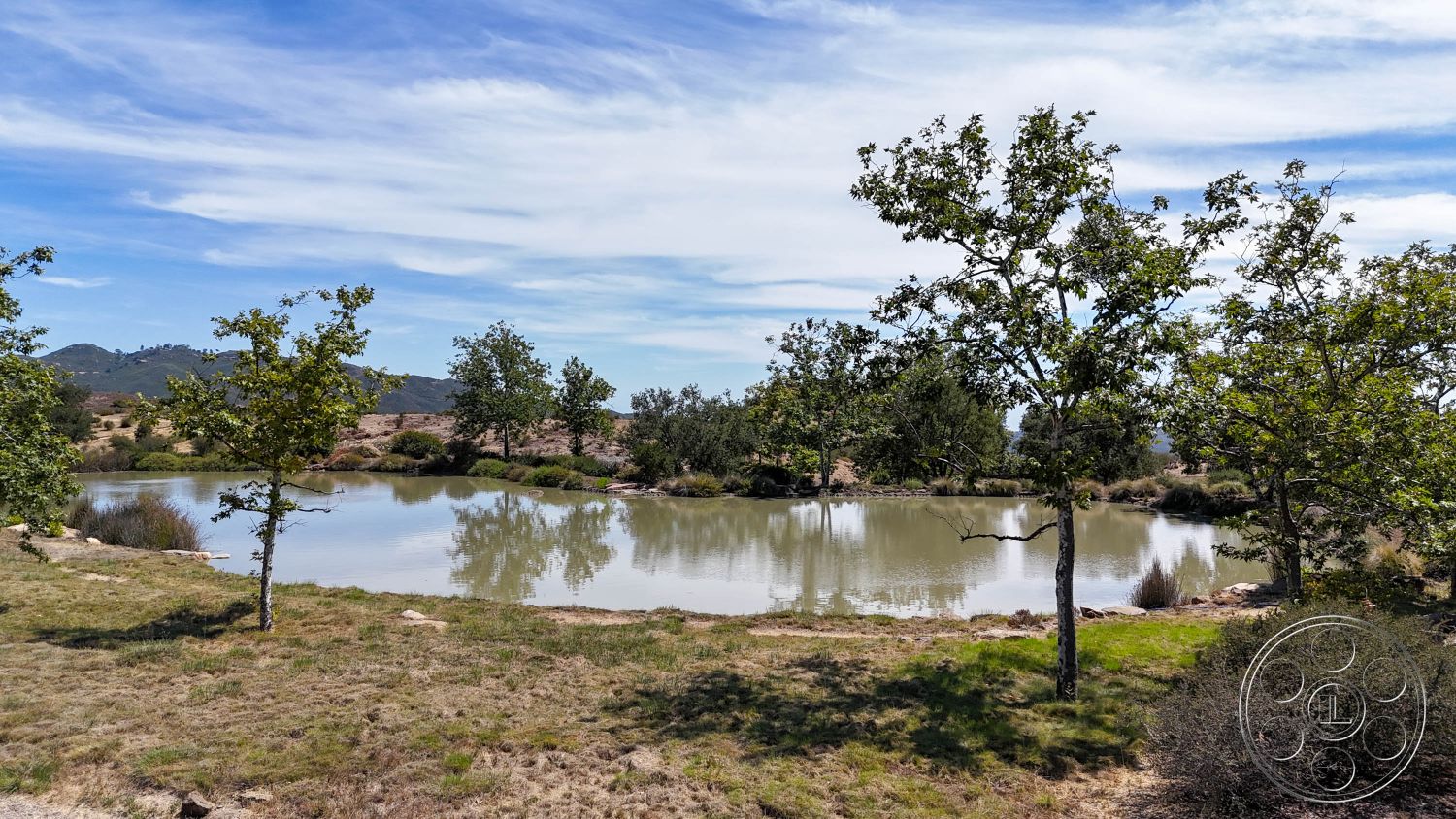 Eagle Feather - mountain backdrop, rock formations, lush vegetation, deciduous trees, open sky, rural environment, landscape setting, natural pond, surrounding grassland, tranquil waters