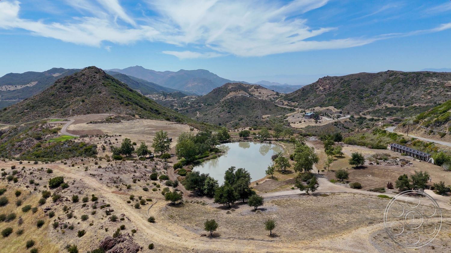 Eagle Feather - exterior, natural landscape, blue sky, dry grass, rocky ground, mountain views, open field, undulating terrain, scattered trees, dirt access road, pond area, cloud patterns