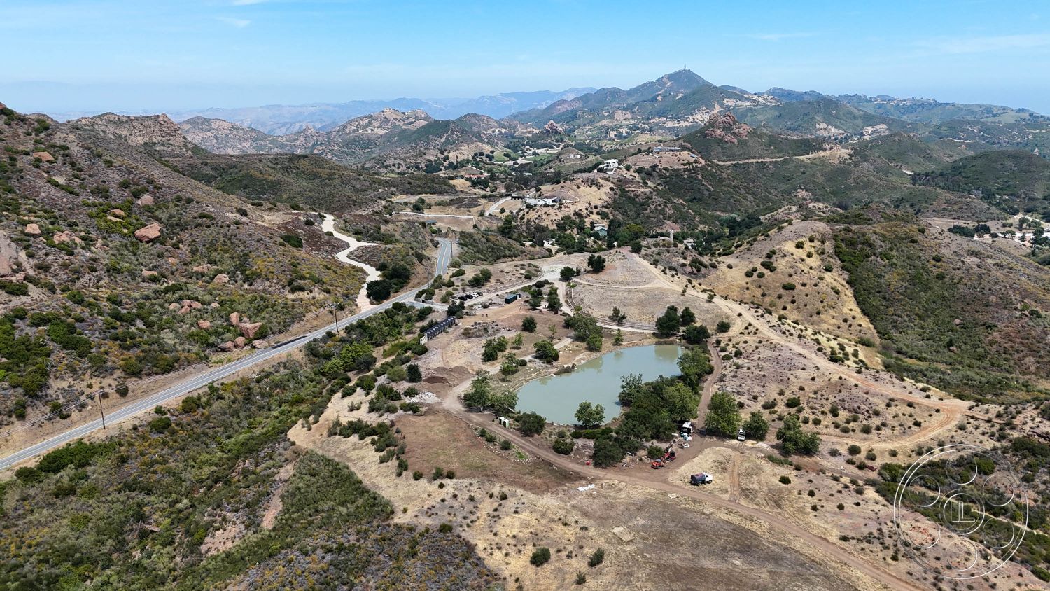 Eagle Feather - exterior, natural landscape, rocky terrain, dirt road, open sky, scattered trees, gentle slopes, mountain setting, pond landscape, vegetated hillsides, residential homes in distance, undulating landforms