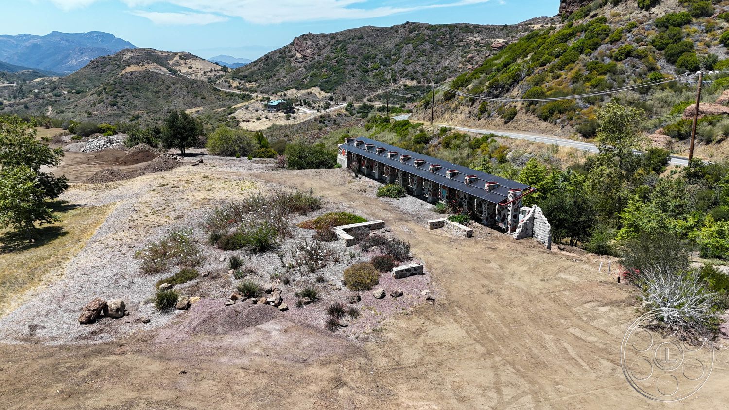 Eagle Feather - exterior, clear blue sky, natural earth tones, surrounding hills, stone retaining wall, mountain landscape, flat roof design, scattered boulders, undisturbed dirt lot, low shrub landscaping, simple building outline, open terrain