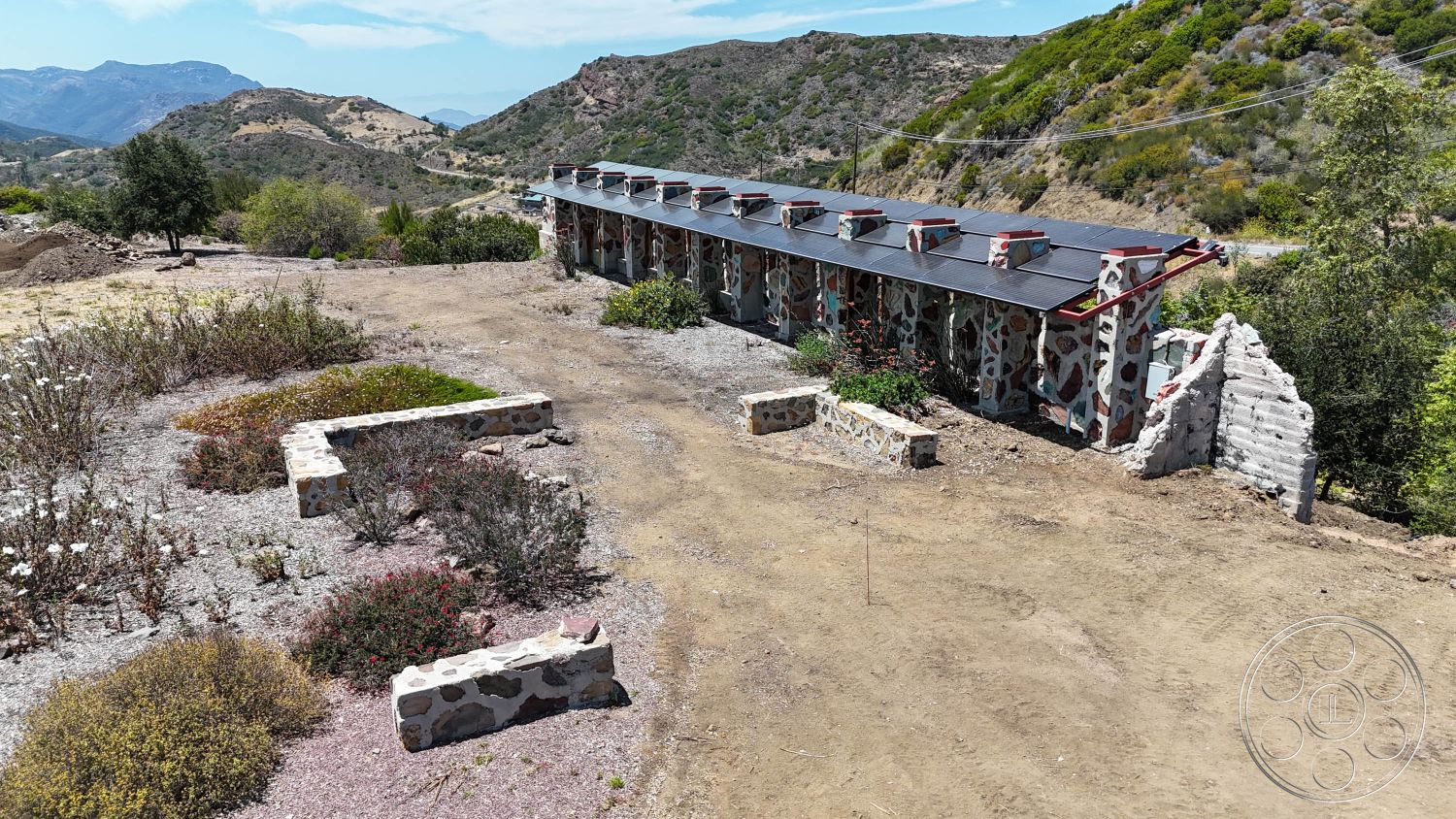 Eagle Feather - exterior, landscaped garden, mountain view, stone walls, garden pathways, sloped metal roof, concrete foundation, textured natural stone, natural hillside setting, open terrain, rustic stone planters, urban homestead, minimal maintenance landscaping, compact modern construction