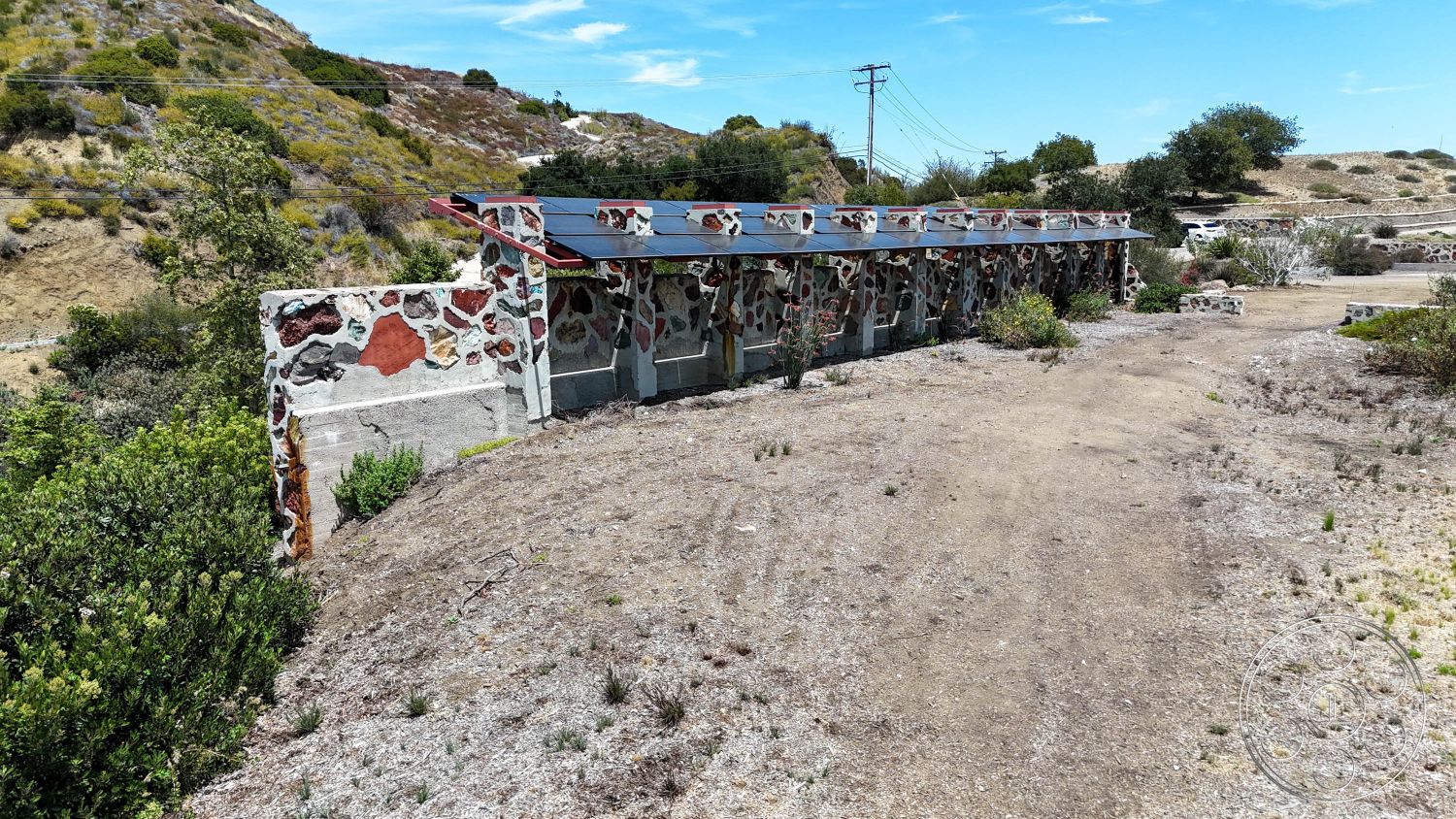 Eagle Feather - exterior, surrounding hillside, minimal vegetation, flat roof design, concrete foundation, rectangular building shape, stone walls with natural rock aggregate, landscaped desert environment, accented wall with colorful stone, outdoor area with sparse plant life