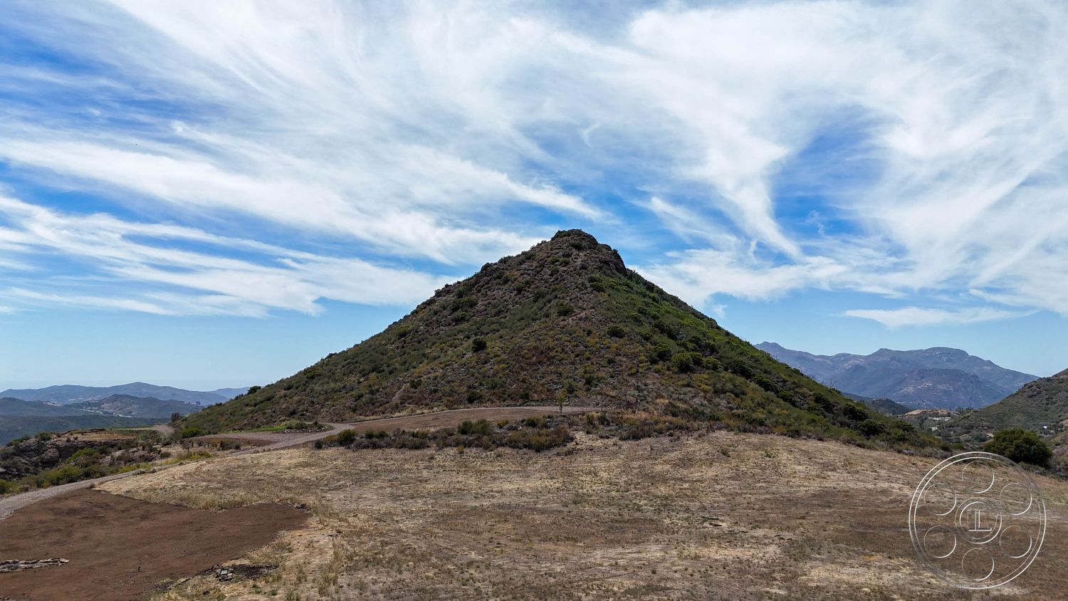 Eagle Feather - exterior, dirt path, natural vegetation, mountain backdrop, rural environment, undulating terrain, arid landscape, cloudy sky, open space setting, grassy hillside, rocky hills landscape