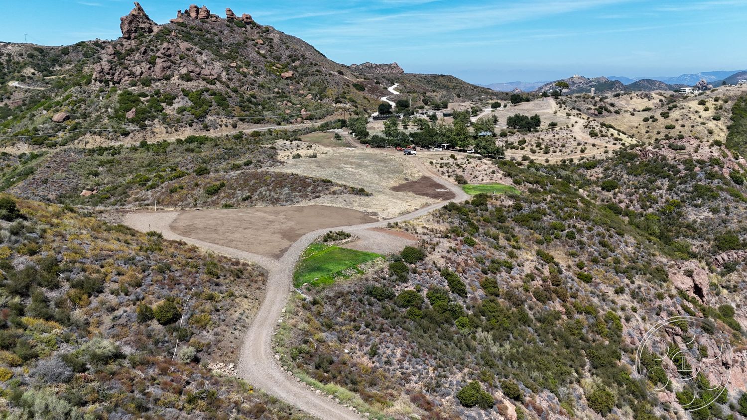 Eagle Feather - sloped terrain, mountain view, clear blue sky, natural landscape setting, dirt access road, rocky outcrops, vegetated hillside, scattered shrubs and greenery, open undeveloped land, dry soil surface, distant residential property