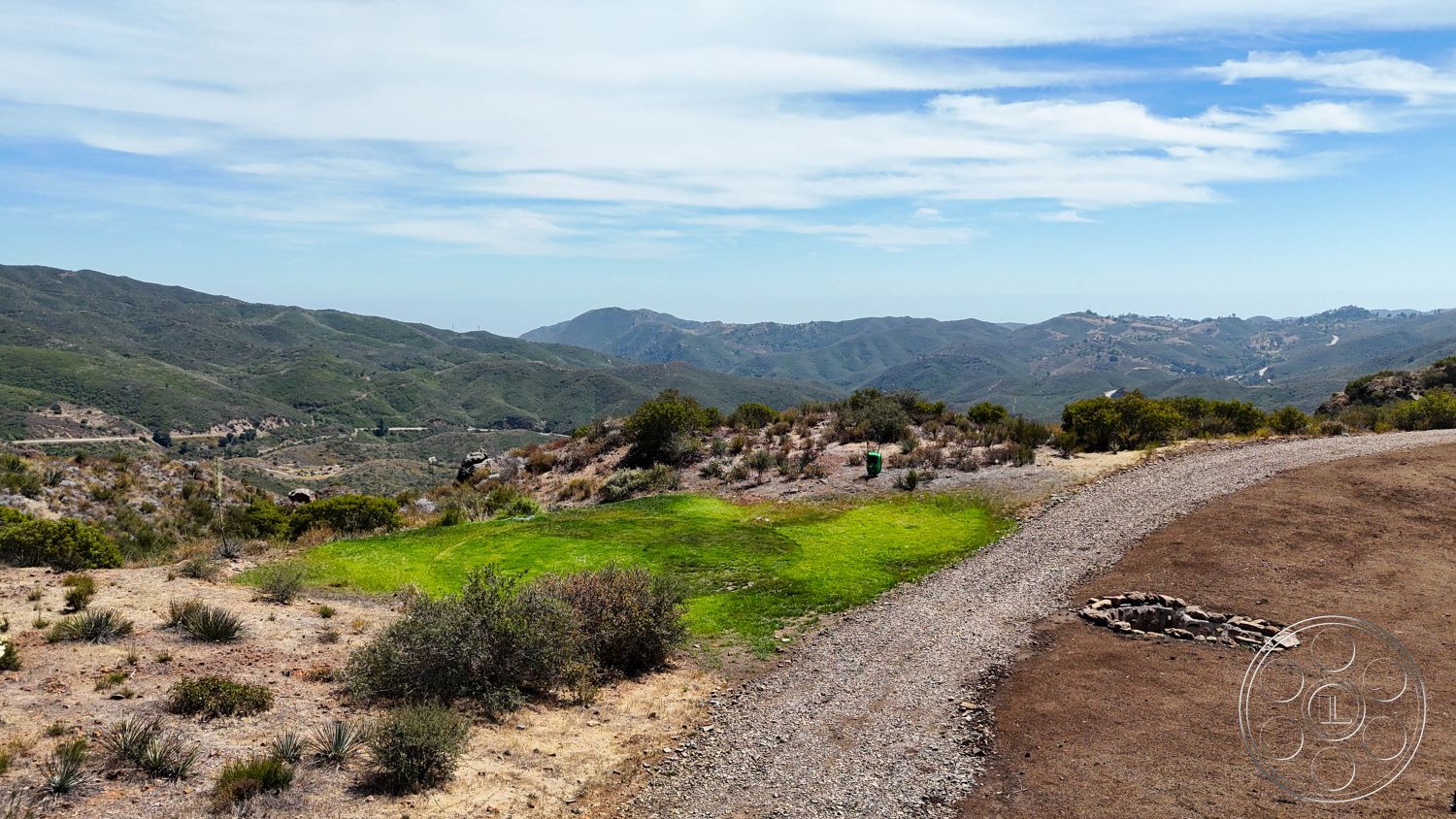 Eagle Feather - exterior, dirt pathway, hillside location, rolling hills, mountain landscape, natural terrain, scattered shrubs, wide open sky, green grass area, gravel ground surface, fire pit stone ring