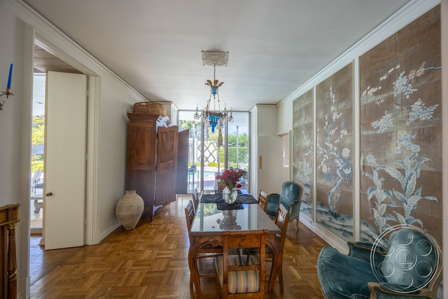 Retro 295 - upholstered dining chairs, wooden dining table, textured wall treatment, large window view, interior dining area, white painted walls, elegant chandelier lighting, parquet wood flooring, floral centerpiece arrangement, exposed door frame, wall-mounted decorative screen, light-filled corridor, decorative wooden armoire