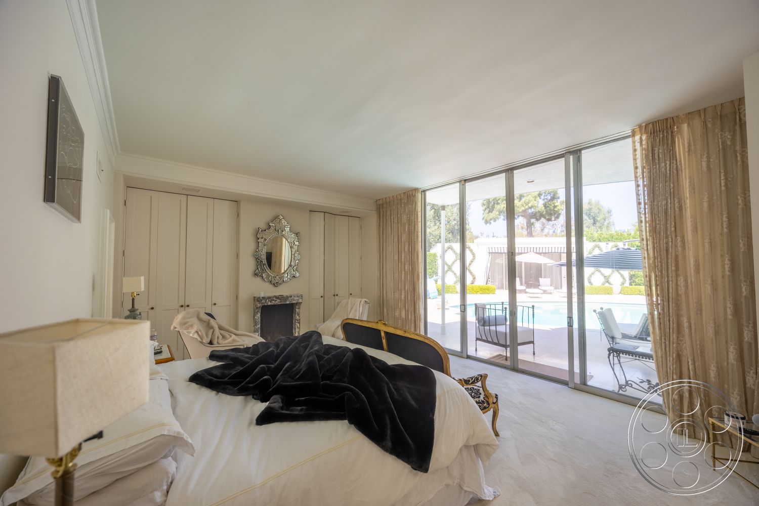 Retro 295 - minimalist decor, plush bedding, floor-to-ceiling windows, vaulted ceiling, framed wall art, king-sized bed, textured plaster walls, outdoor pool view, modern table lamp, wood bedside table, carpet bedroom flooring, sheer curtain drapes, gold trimmed mirror, dark throw blanket, black and white accent chair, well-lit bedroom