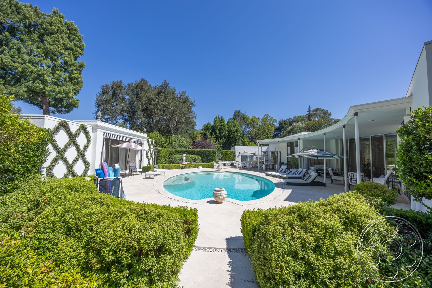 Retro 295 - exterior, landscaped garden, glass sliding doors, contemporary architecture, outdoor lounge area, potted greenery, green hedges, clear blue sky, open-air living space, concrete pool deck, architectural detail, natural stone planters, curved swimming pool, modern home design, tile patio flooring, striped outdoor umbrellas, vaulted rooflines
