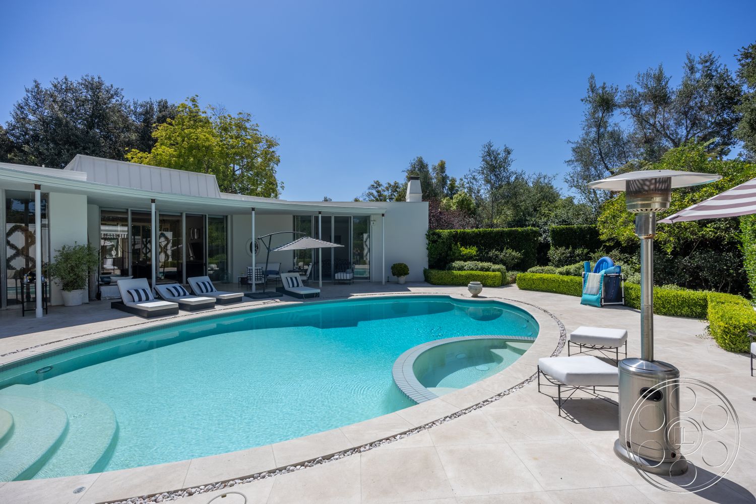 Retro 295 - exterior, white stucco walls, glass sliding doors, modern architectural style, sunshade umbrella, concrete pool deck, curved pool, metal patio heater, landscaped garden with hedges, rectangular patio, stone border around pool, lounge chairs with cushions, heat reflective glass, vinyl lounge chair cushions, tiled coping around pool