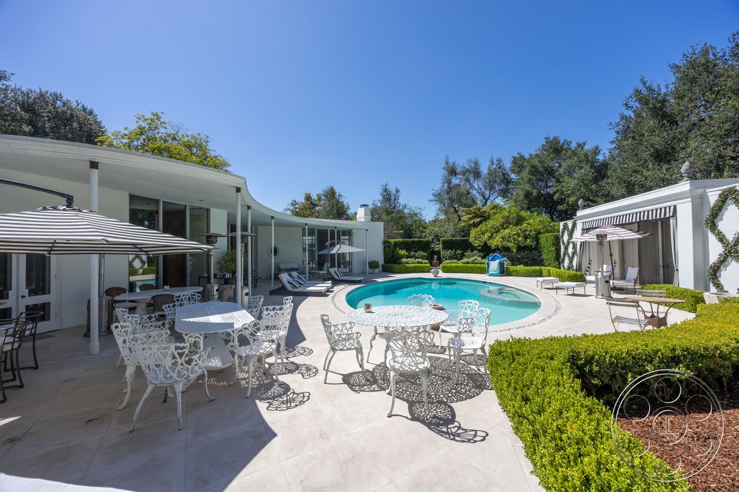 Retro 295 - exterior, glass sliding doors, rectangular swimming pool, concrete patio flooring, natural light environment, white wrought iron patio furniture, curved architectural walls, green hedges landscaping, overhead fabric umbrellas, modern style home