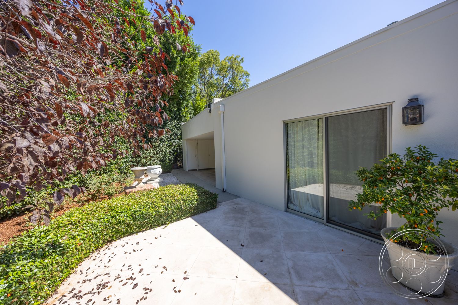 Retro 295 - exterior, white stucco walls, glass sliding doors, vibrant foliage, stone planter, concrete patio flooring, curved garden pathway, leaf-strewn pathway, green shrubbery landscaping, decorative outdoor light fixture