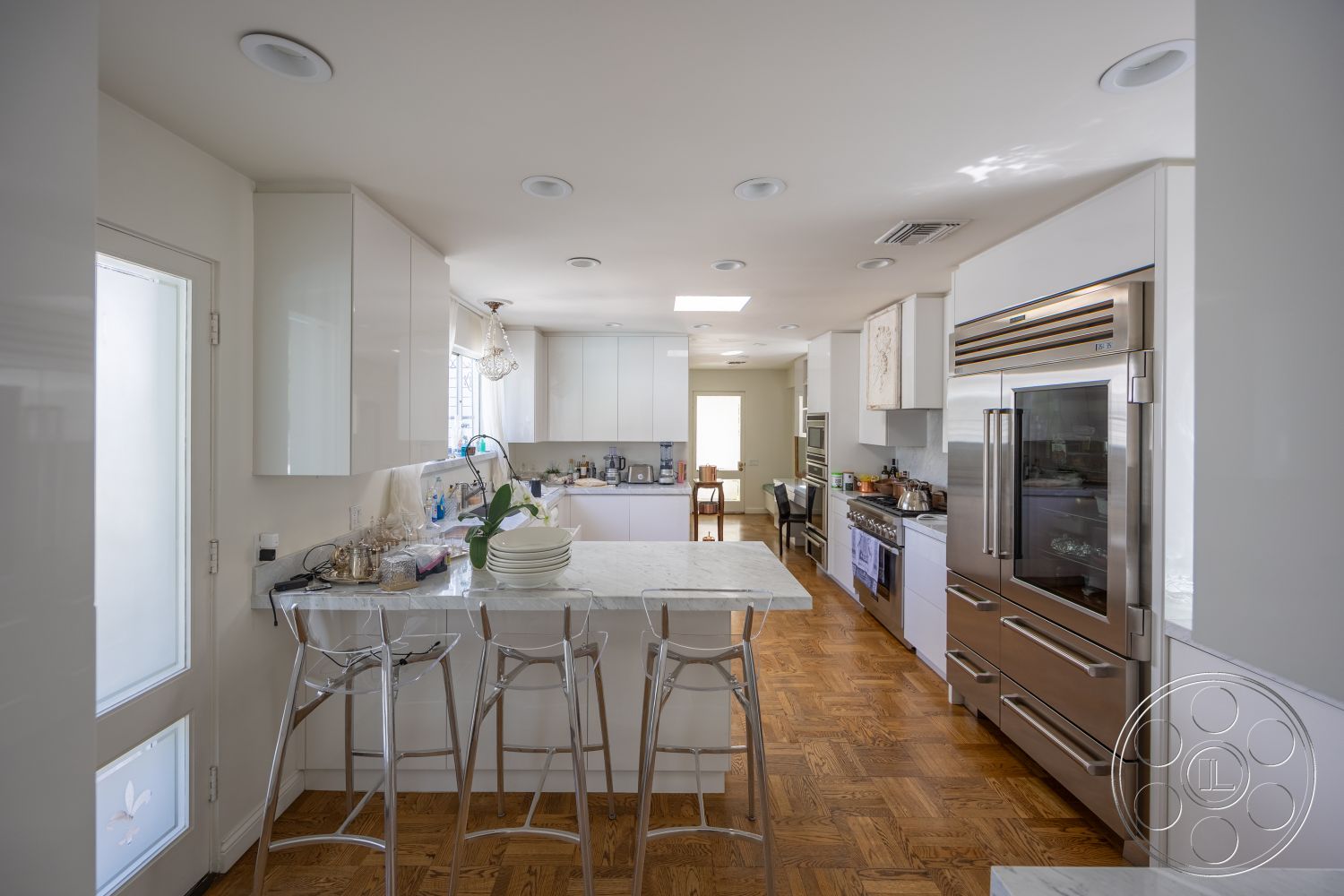 Retro 295 - open concept layout, white cabinetry, bright natural lighting, glass cabinet doors, stainless steel refrigerator, modern bar stools, painted walls, stainless steel oven, hardwood parquet flooring, marble kitchen island, skylight overhead, kitchen workspace