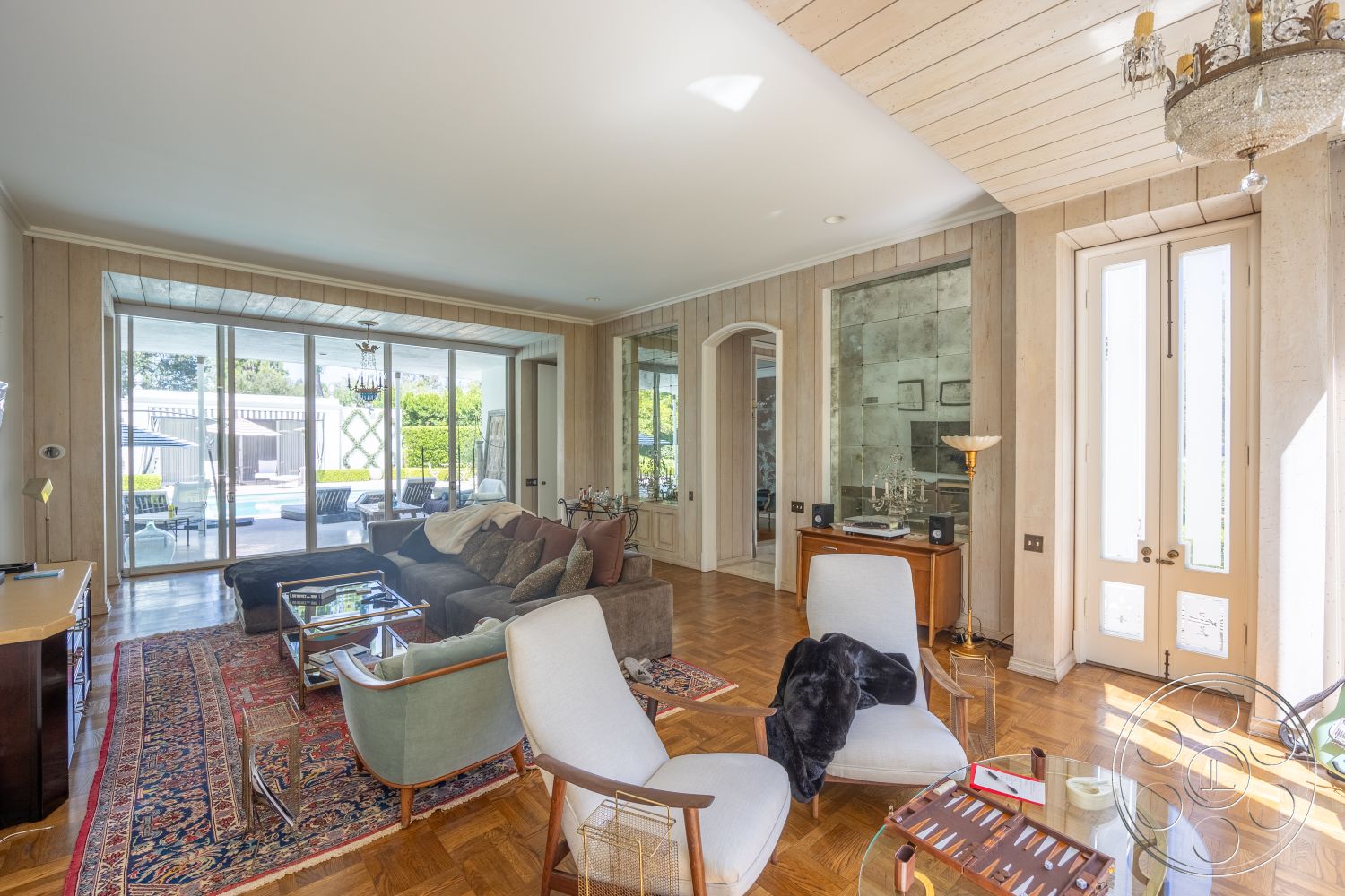 Retro 295 - neutral color palette, decorative area rug, indoor plants, open floor plan, soft lighting, glass coffee table, plush sectional sofa, arched doorways, textured plaster walls, luxurious living room, elegant chandelier, floor-to-ceiling glass windows, wood paneling walls, herringbone hardwood floors, vintage wooden sideboard