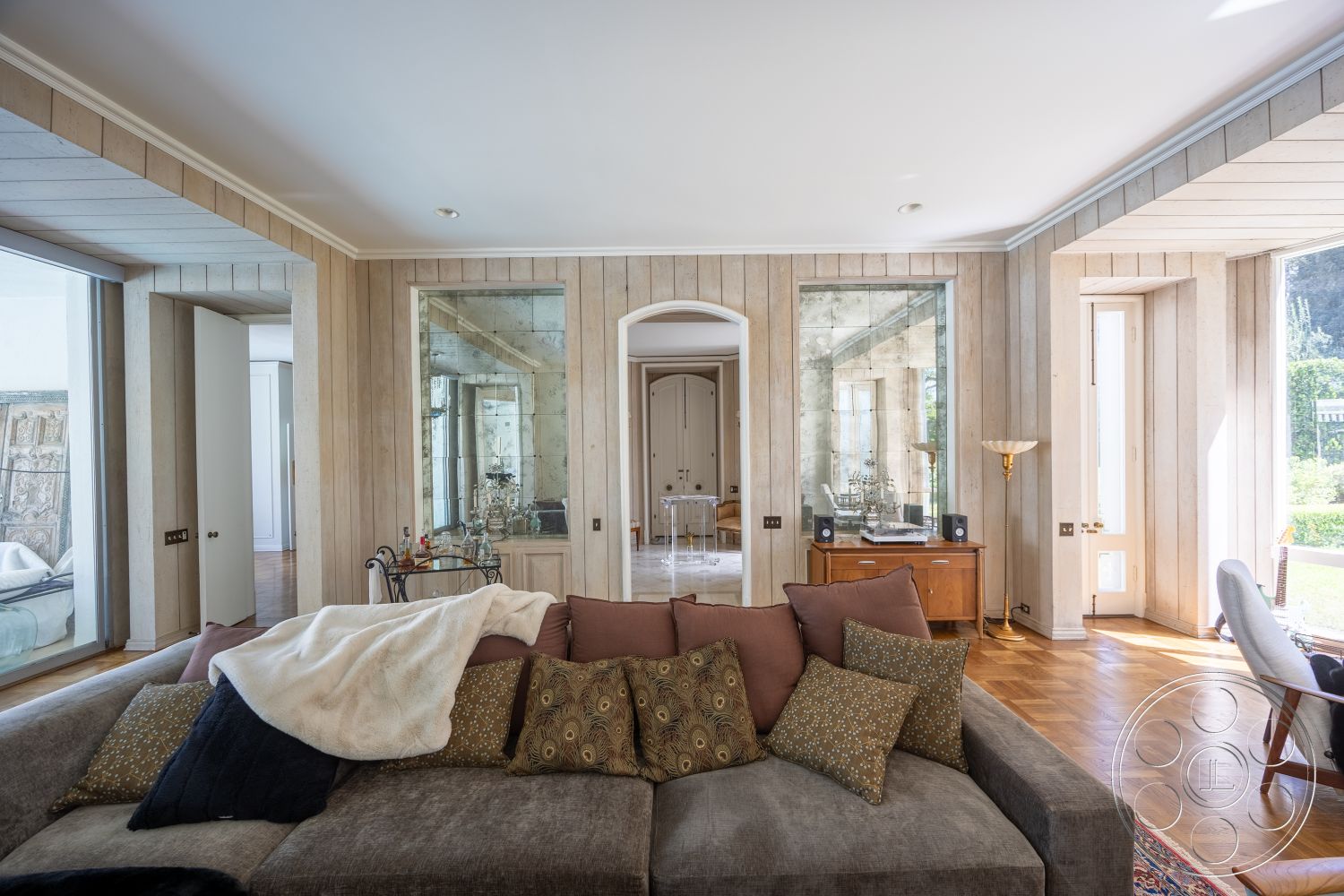 Retro 295 - minimalist decor, natural light, hardwood flooring, open floor plan, modern design elements, floor-to-ceiling windows, arched doorways, decorative throw pillows, framed mirrors, gold floor lamp, textured wood paneling, contemporary living area, grey upholstered sofa