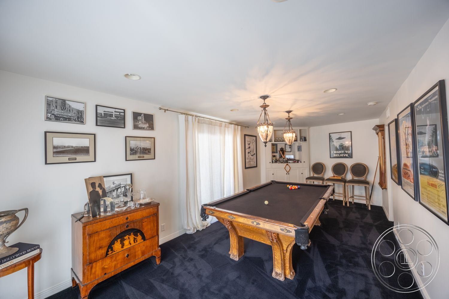 Retro 295 - bar stools, built-in cabinetry, white painted walls, dark carpet flooring, sheer curtain window treatments, chandelier lighting fixtures, wooden billiard table, vintage framed wall art, wooden decorative chest
