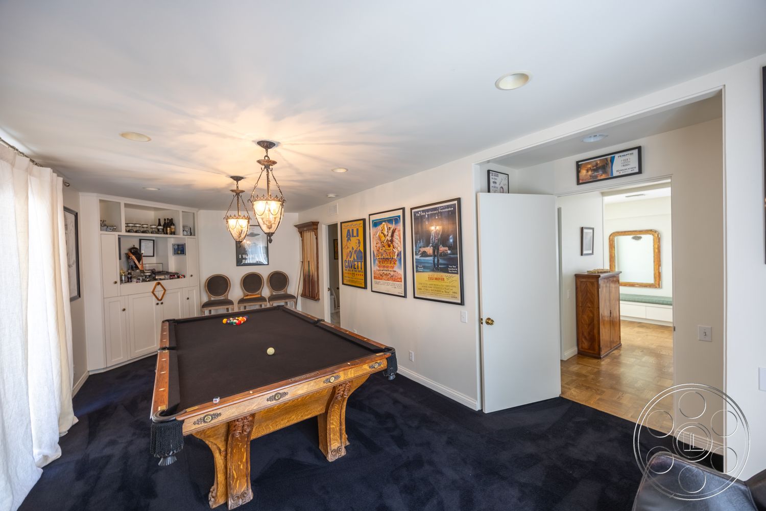 Retro 295 - arched doorways, wood paneling accents, dark carpet flooring, built-in white cabinetry, textured white ceiling, black felt billiard table, wood billiard table legs, traditional brass light fixtures, framed movie posters, dark wood sideboard, elegant seating chairs