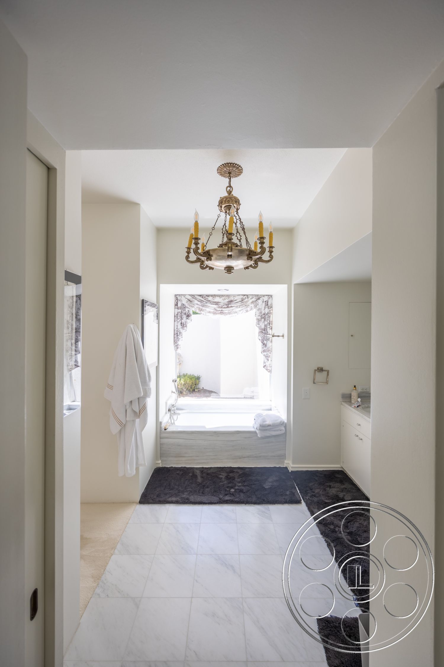 Retro 295 - natural light from windows, built-in cabinetry, spa-like bathroom ambiance, glass shower doors, white painted walls, crown molding details, marble tile flooring, chandelier lighting fixture, open doorway to outdoor space, dark area rugs