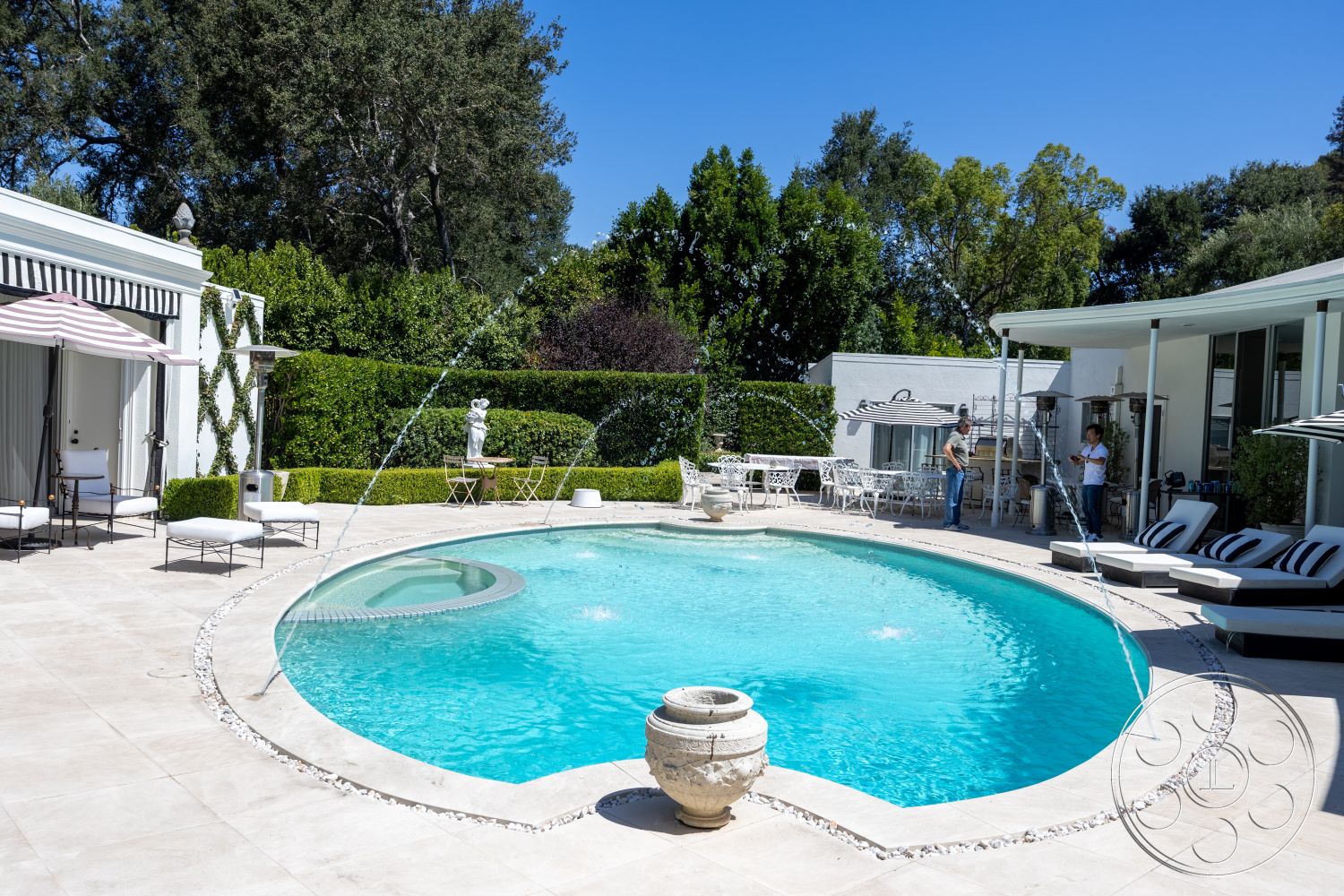 Retro 295 - exterior, white stucco walls, modern outdoor furniture, pool area, garden setting, concrete pool deck, metal outdoor chairs, oval swimming pool, surrounding lush greenery, sunny outdoor environment, stone pool border, paved patio flooring, decorative stone fountain, striped canvas umbrellas