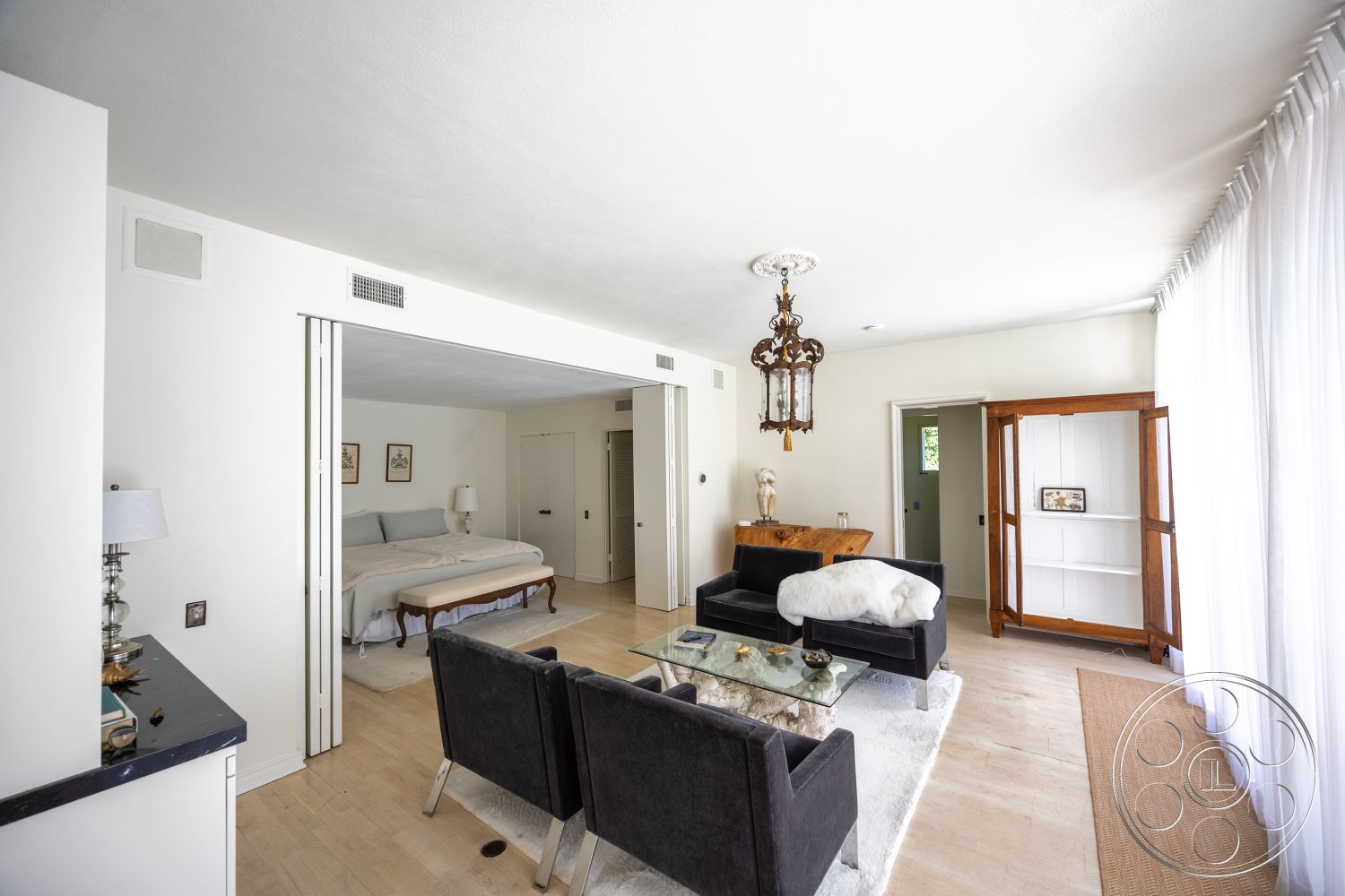 Retro 295 - hardwood flooring, minimalist design, glass coffee table, textured plaster ceiling, light wood floor, traditional chandelier, open plan layout, white painted walls, framed artwork on walls, floor-to-ceiling sheer curtains, neutral bedding, black velvet armchairs, wood display cabinet