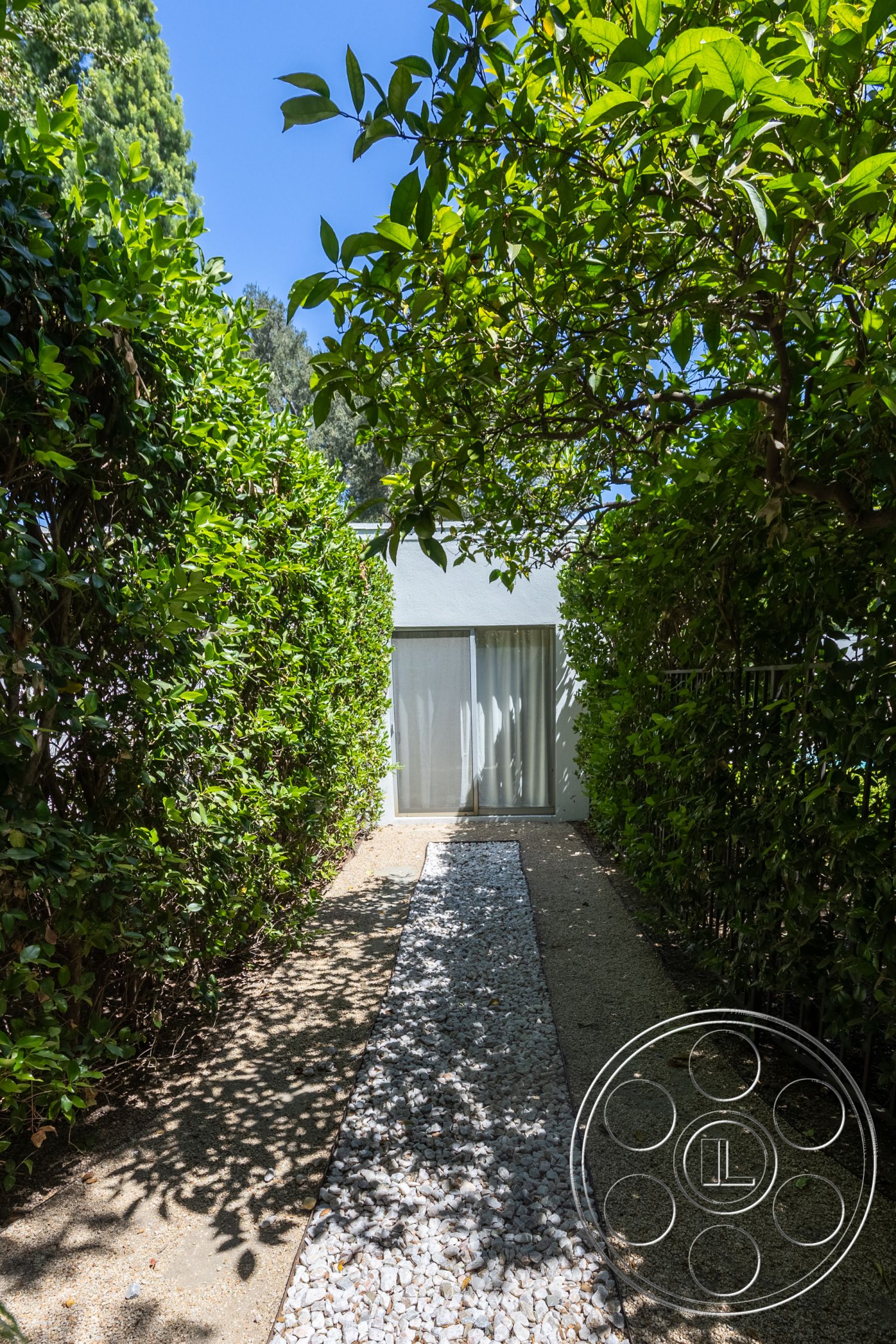 Retro 295 - exterior, landscaped garden, glass sliding doors, gravel pathway, planted greenery, white facade, sunny outdoor setting, hedge border, concrete pathway base