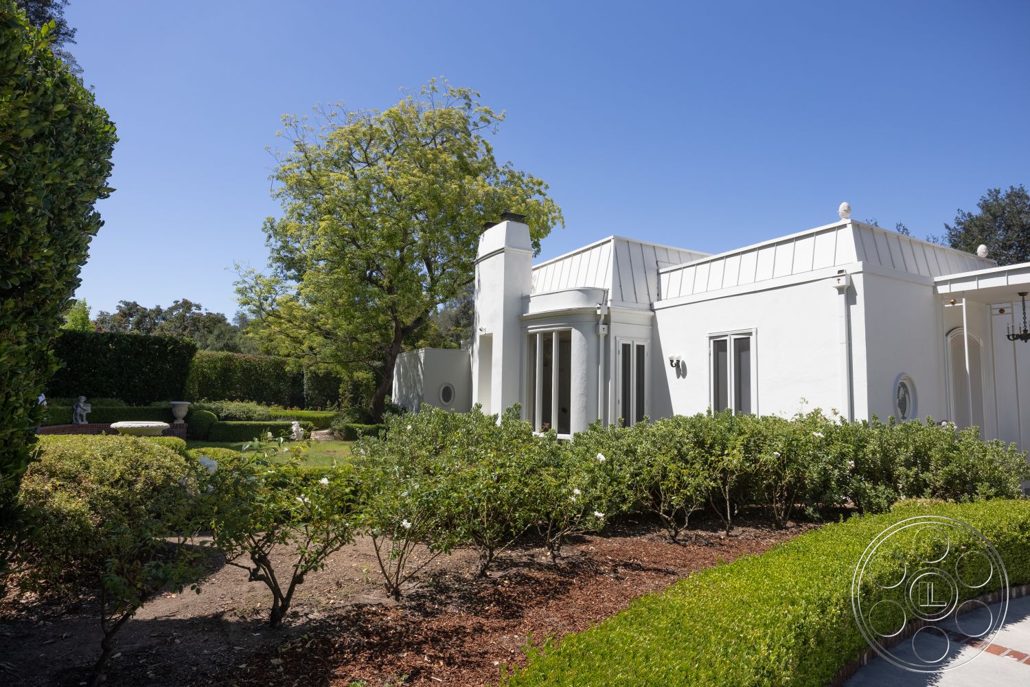 Retro 295 - exterior, white stucco walls, modern architectural style, landscaped garden setting, curved garden path, blooming flower beds, metal roof with standing seams, manicured hedge borders, decorative brick garden accents, large windows with frames