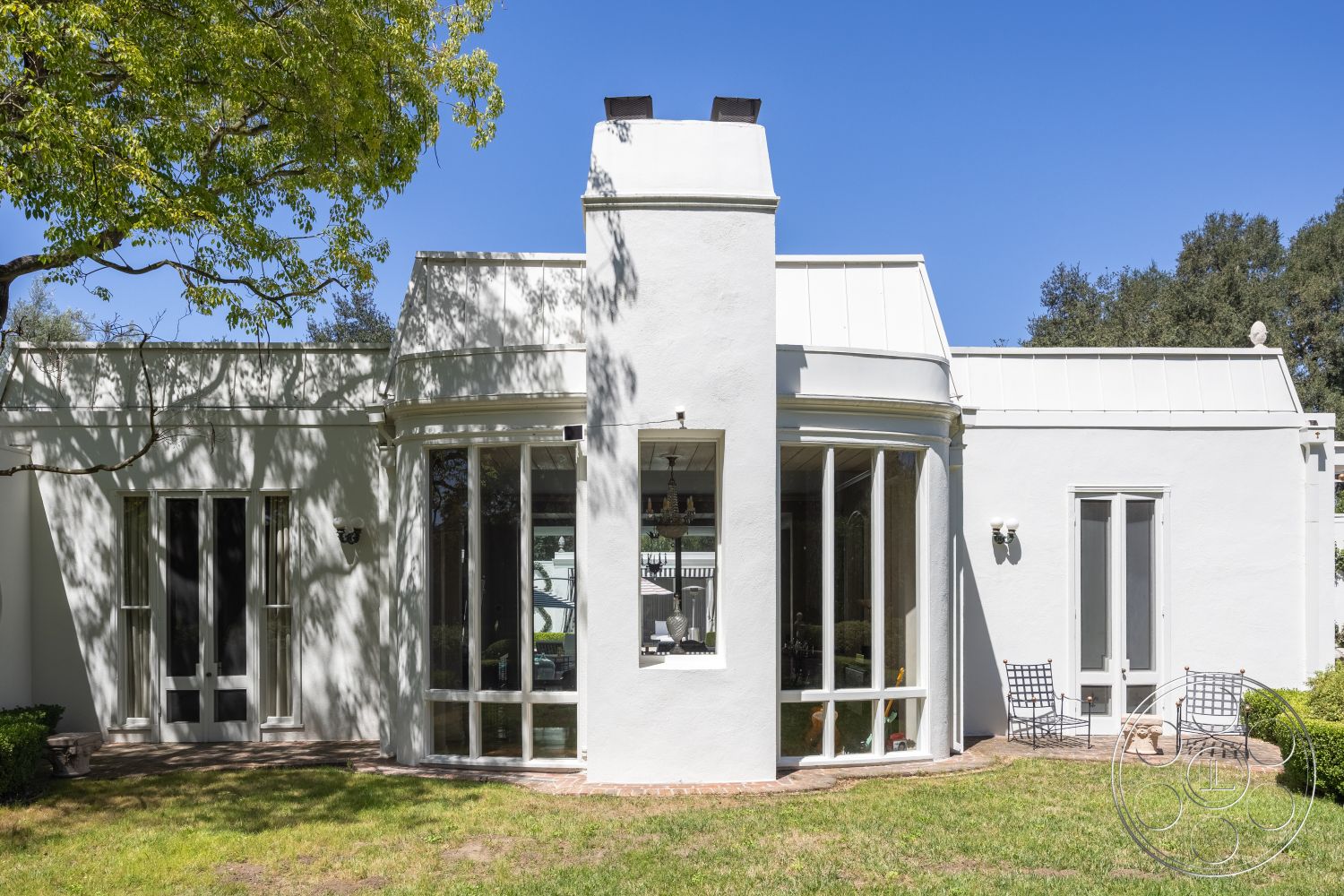 Retro 295 - exterior, white stucco walls, modern design, large glass windows, outdoor seating area, surrounding greenery, symmetrical facade, landscaped garden area, curved architectural forms, double-door entry, flat metal roof, brick patio base