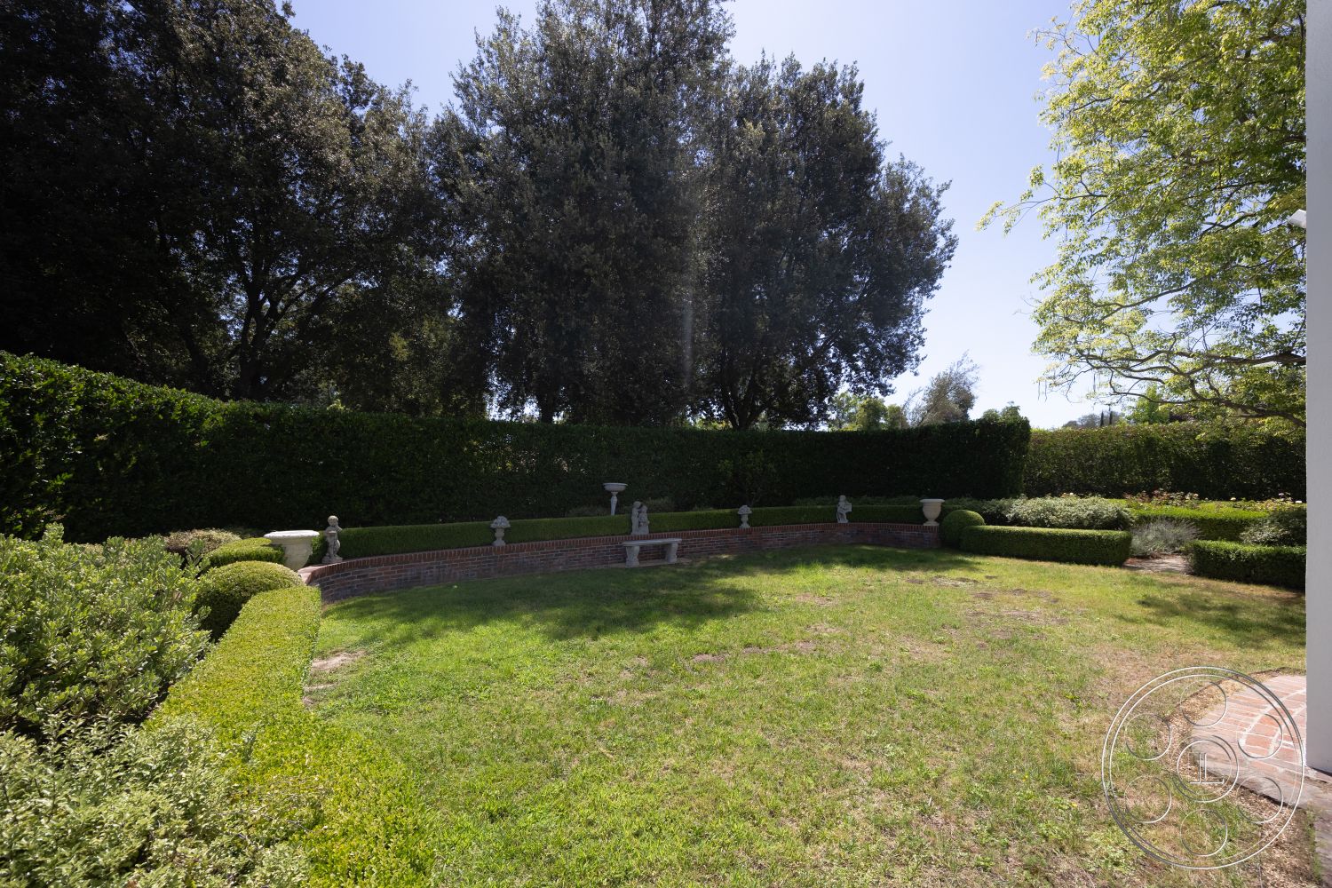 Retro 295 - exterior, landscaped garden, green lawn, garden pathway, lush vegetation, manicured hedges, stone planter boxes, tall trees providing shade, circular lawn area, decorative garden statues, brick border garden wall