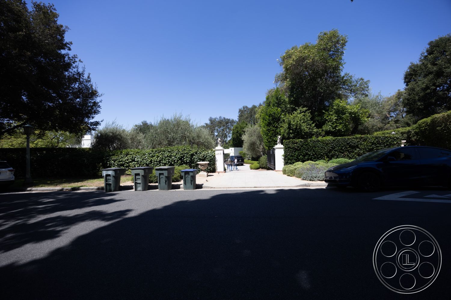 Retro 295 - asphalt driveway, outdoor lighting fixtures, lush green trees, landscaped garden area, exterior residential setting, modern gate entrance, tall hedge privacy wall, concrete path to entrance, vibrant shrubs
