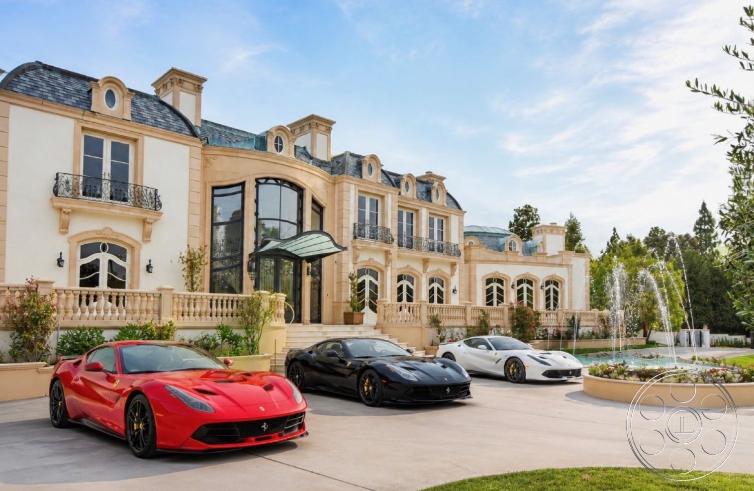 Tiffany Estate - exterior, circular driveway, manicured lawn, fountain feature, planted garden beds, concrete driveway surface, glass entrance doors, slate roof tiles, limestone exterior walls, arched windows with black wrought iron railings, ornate stone balcony, luxury sports cars
