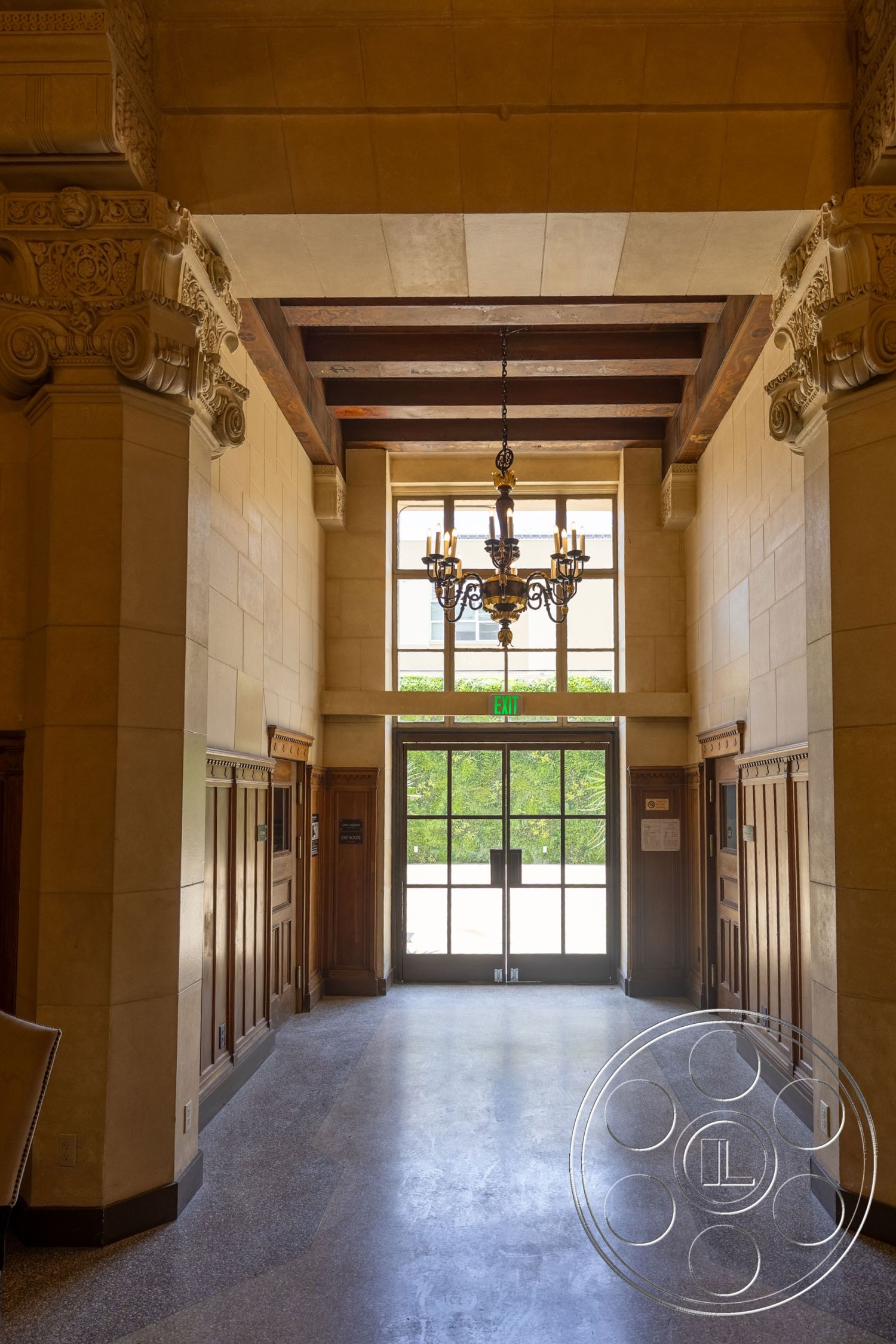 The Plaza - wood paneling, chandelier lighting, arched doorways, textured plaster walls, polished terrazzo flooring, ornate ceiling details, exposed wood ceiling beams, large pane windows, classical architectural style
