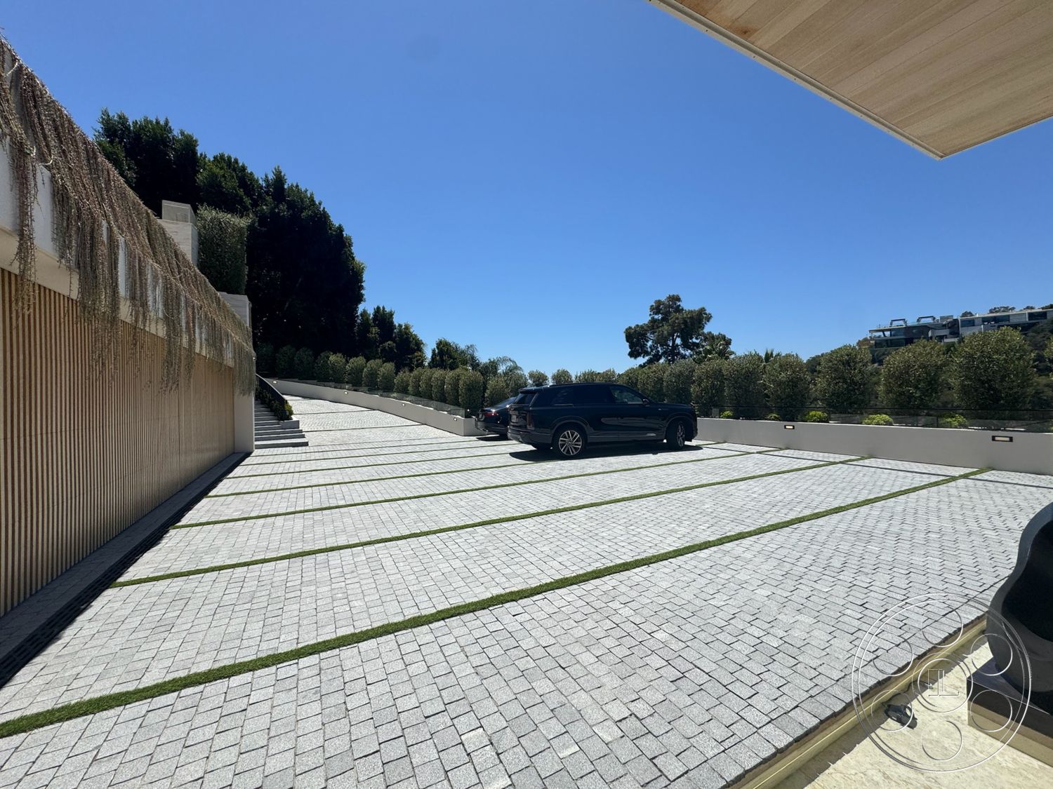 Chalon Estate - exterior, paved driveway, modern landscaping, urban setting, green grass strips, textured wood paneling, sunny outdoor environment, grey stone pavers, stepped driveway layout, garden hedges