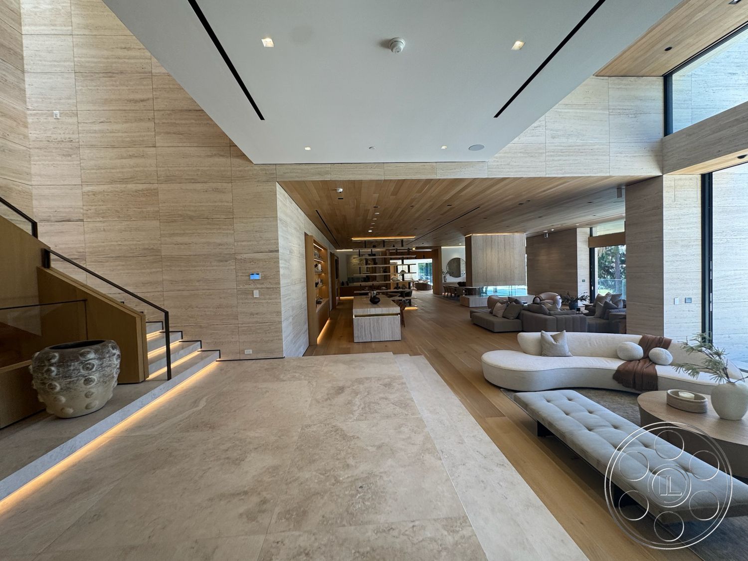 Chalon Estate - neutral color palette, contemporary style, light marble flooring, large floor-to-ceiling windows, glass partition walls, natural light-filled space, built-in shelving unit, modern furniture design, open floor plan living space, floating stairs with glass railings, integrated LED lighting, light-colored wood paneling ceiling, textured wood accent walls, soft-toned upholstered seating area