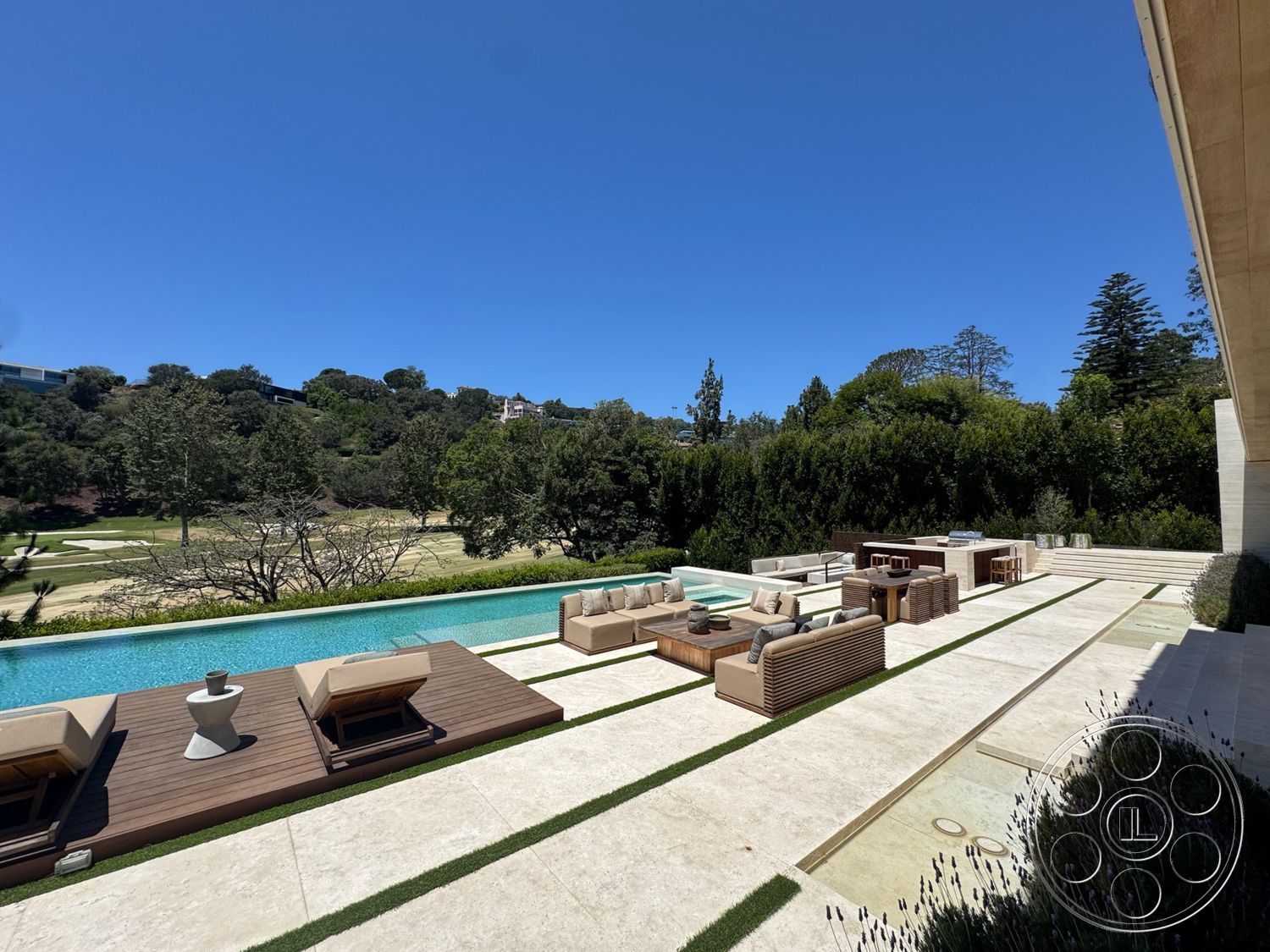 Chalon Estate - exterior, clear blue sky, rectangular pool, minimalist garden, grass landscaping, stone pool deck, concrete patio flooring, modern outdoor seating area, wooden deck platform, stainless steel outdoor kitchen, rolling hillside view, tree line border, composite outdoor furniture