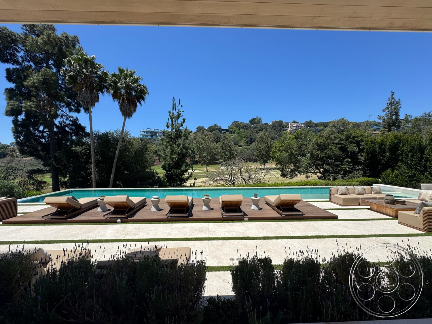 Chalon Estate - exterior, modern architecture, palm trees, rectangular swimming pool, open outdoor space, views of greenery, concrete pool deck, mountainous landscape, outdoor seating area with cushions, wooden sun loungers, sunny sky, gray stone patio flooring, low wooden table, landscaped garden with bushes, mature trees in the background