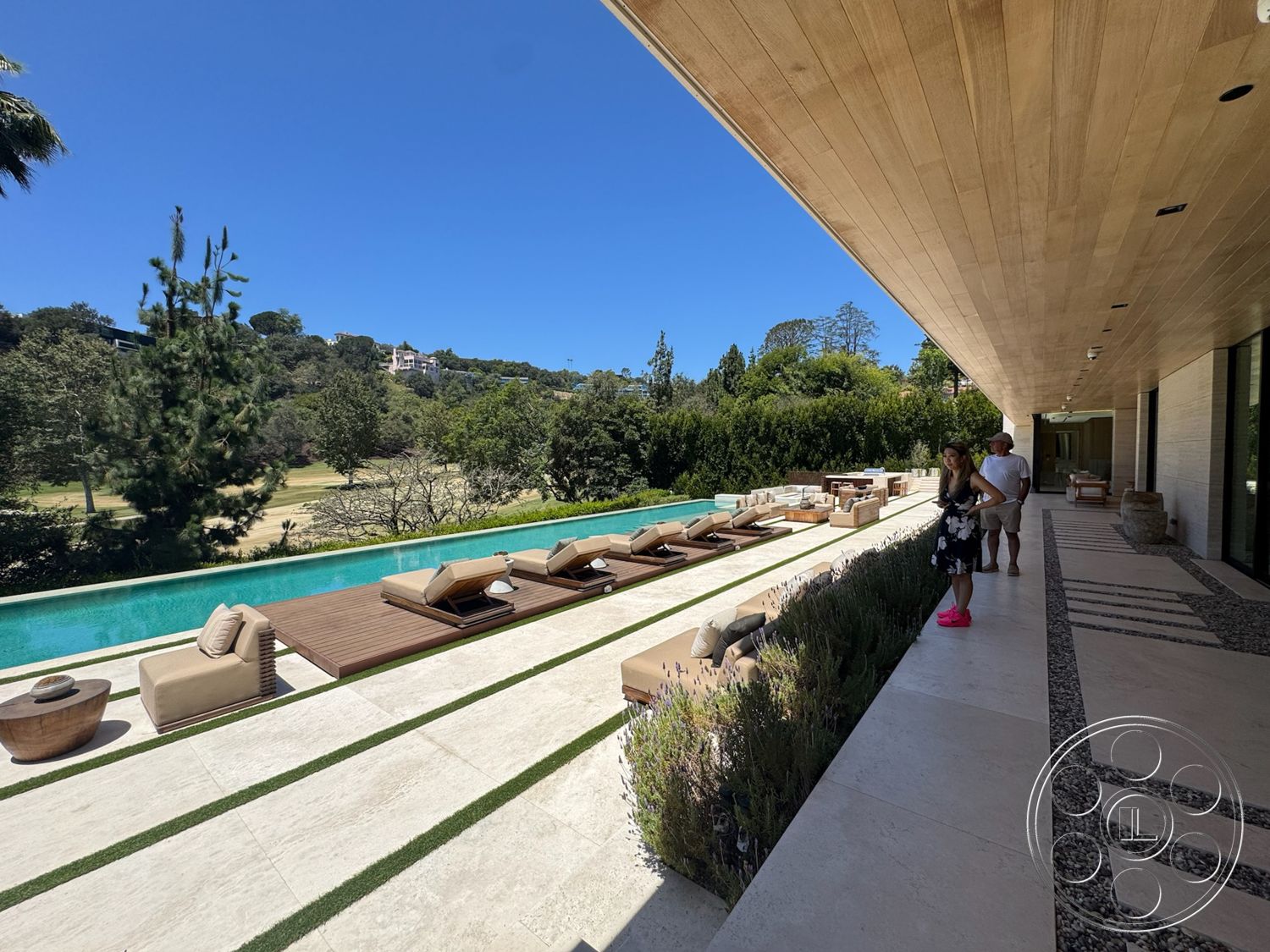 Chalon Estate - exterior, glass sliding doors, rectangular swimming pool, indoor-outdoor living, wooden lounge chairs, decorative stone planters, stone patio flooring, concrete pool border, horizontal wood slat fencing, green landscape setting, wood ceiling paneling, striped garden pathway