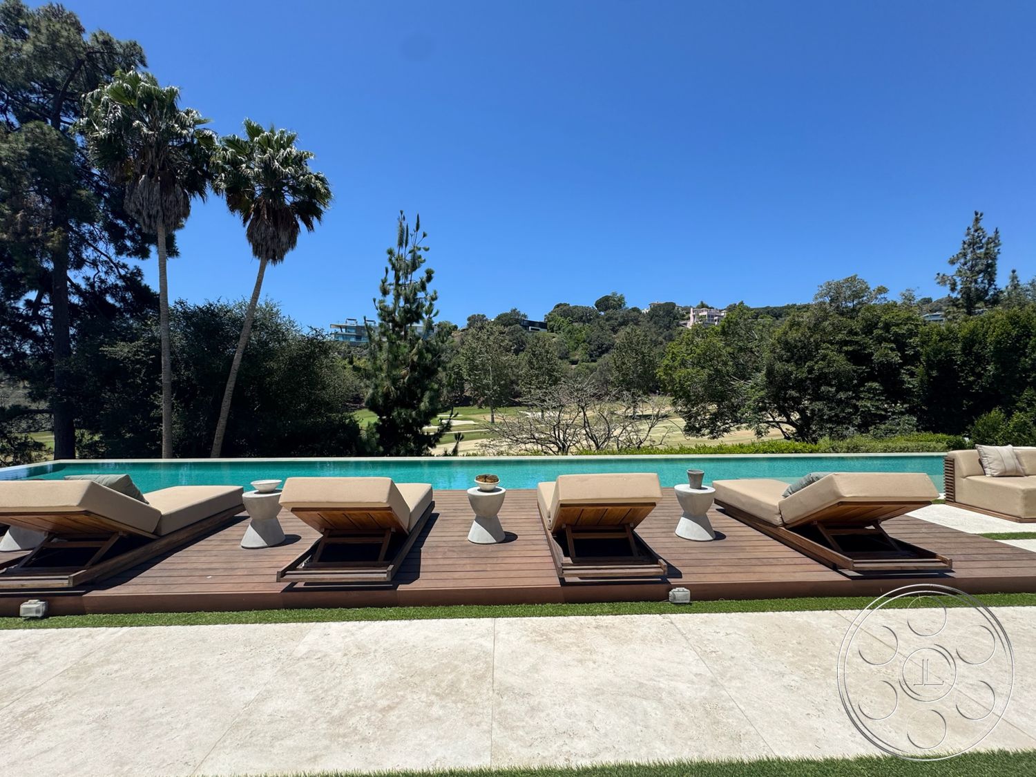 Chalon Estate - exterior, palm trees, sun loungers, concrete pool deck, modern outdoor seating, rectangular infinity pool, glass pool edge, synthetic grass landscaping, wood deck lounge area, dense greenery backdrop