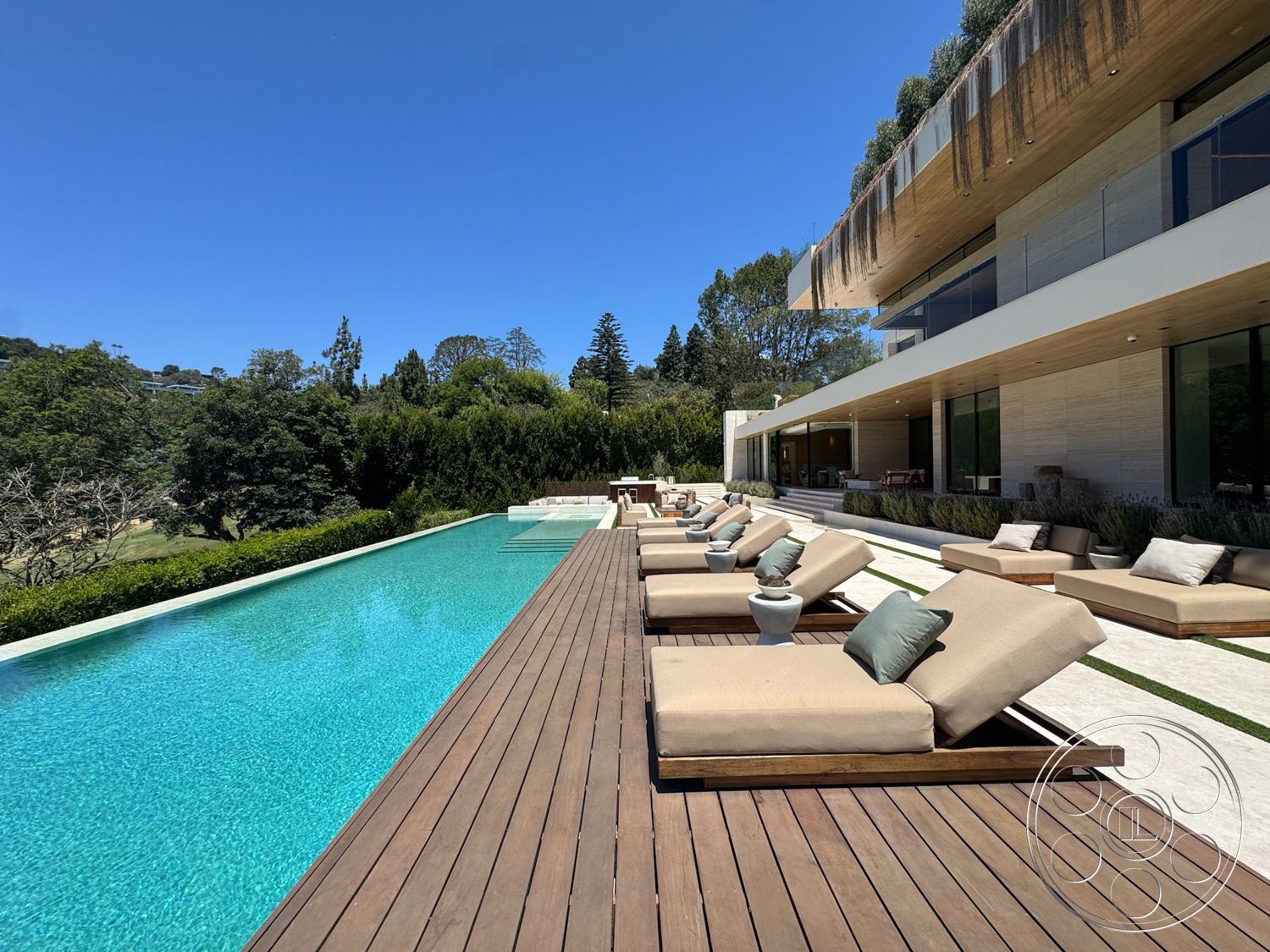 Chalon Estate - exterior, sliding glass doors, wooden deck, floor-to-ceiling windows, outdoor lounge area, modern architectural style, infinity pool, landscape greenery, surrounding trees and shrubs, stone patio flooring, concrete pool border, horizontal wooden planks, sun loungers with cushions